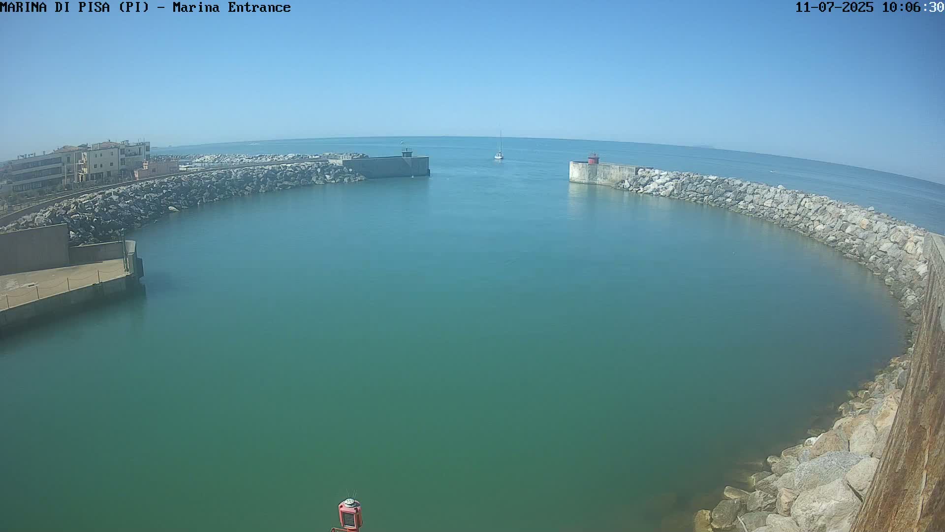 A harbor entrance with calm, teal water is bordered by rock walls under a clear, sunny sky.