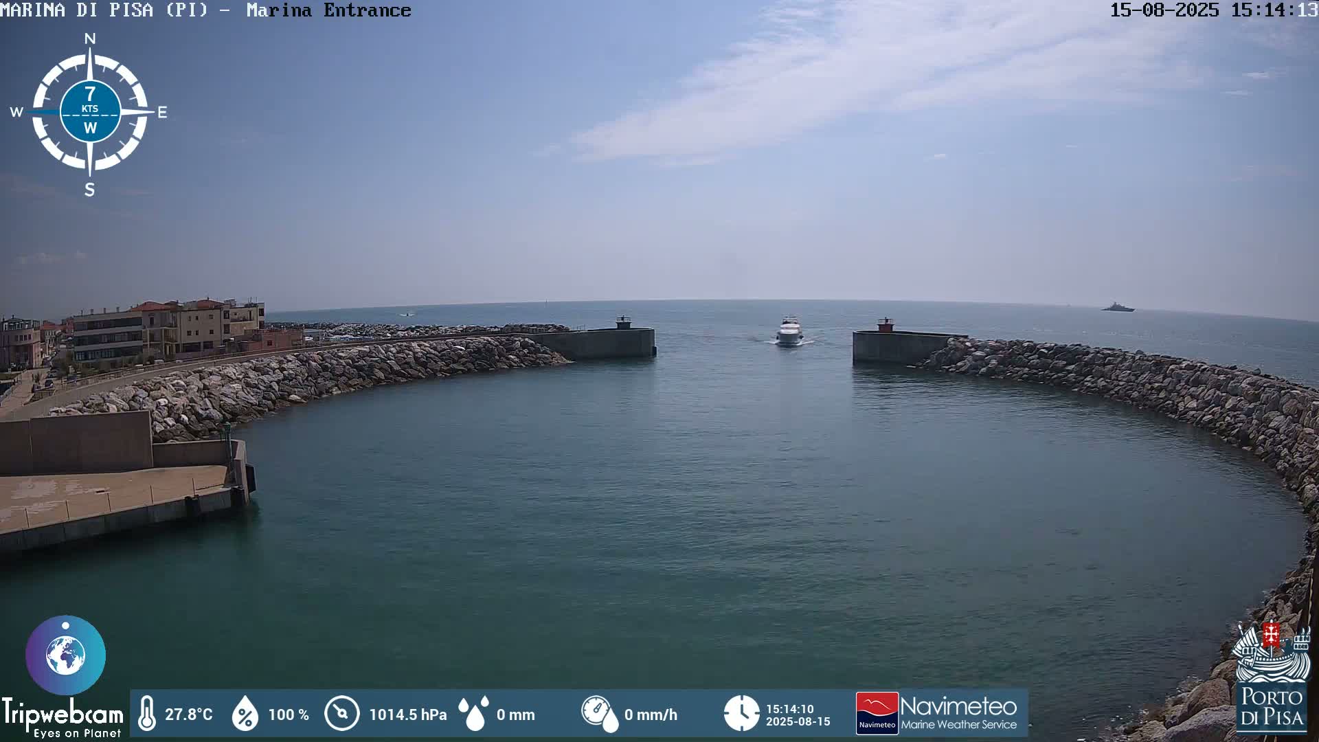 A harbor entrance with calm water under a clear blue sky shows a curved stone breakwater and a distant vessel.