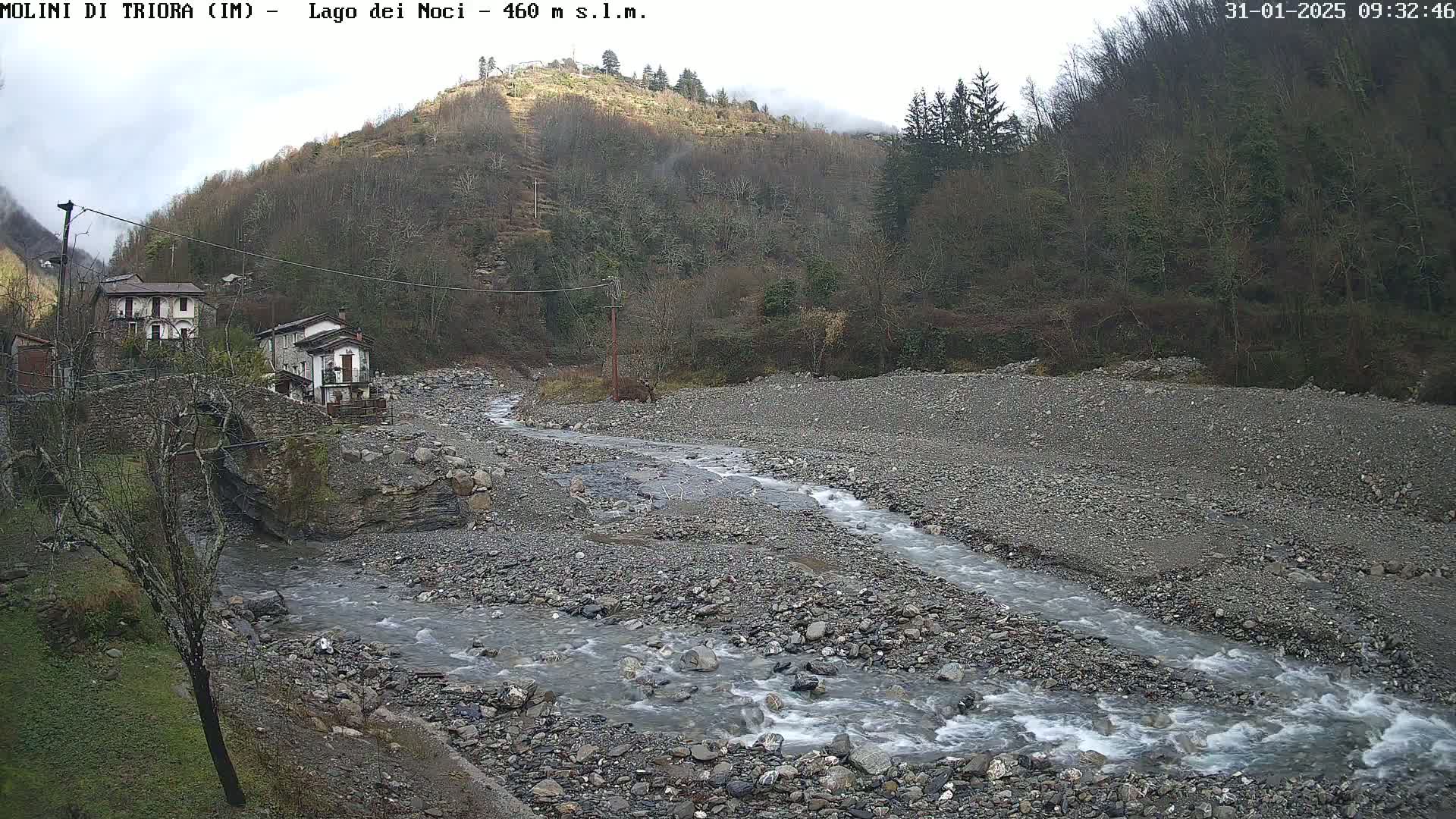 A rocky stream flows through a valley under an overcast sky, past a small village nestled against a hillside.