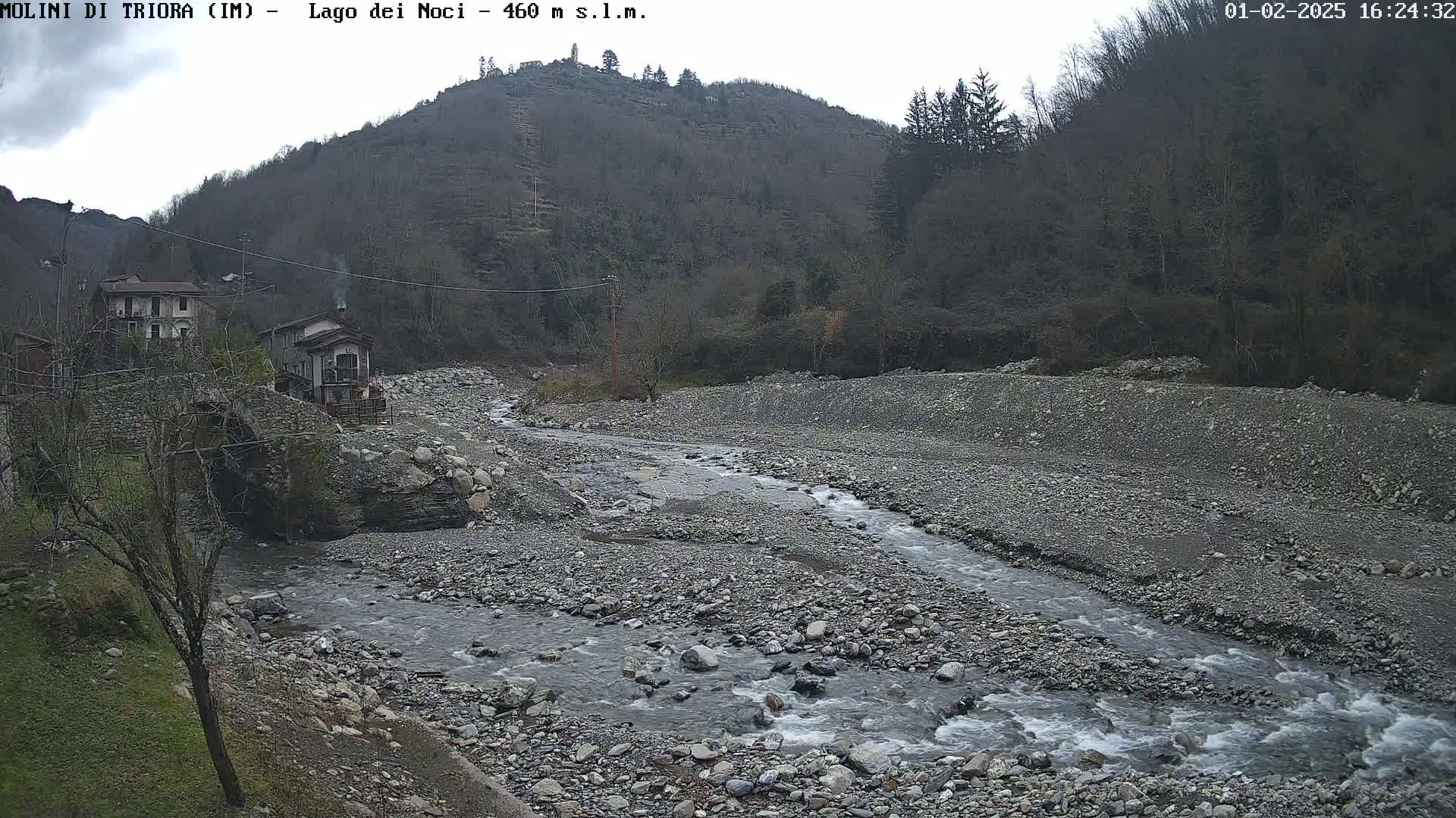 A rocky river flows through a valley under an overcast sky, past a small village nestled against a hillside.