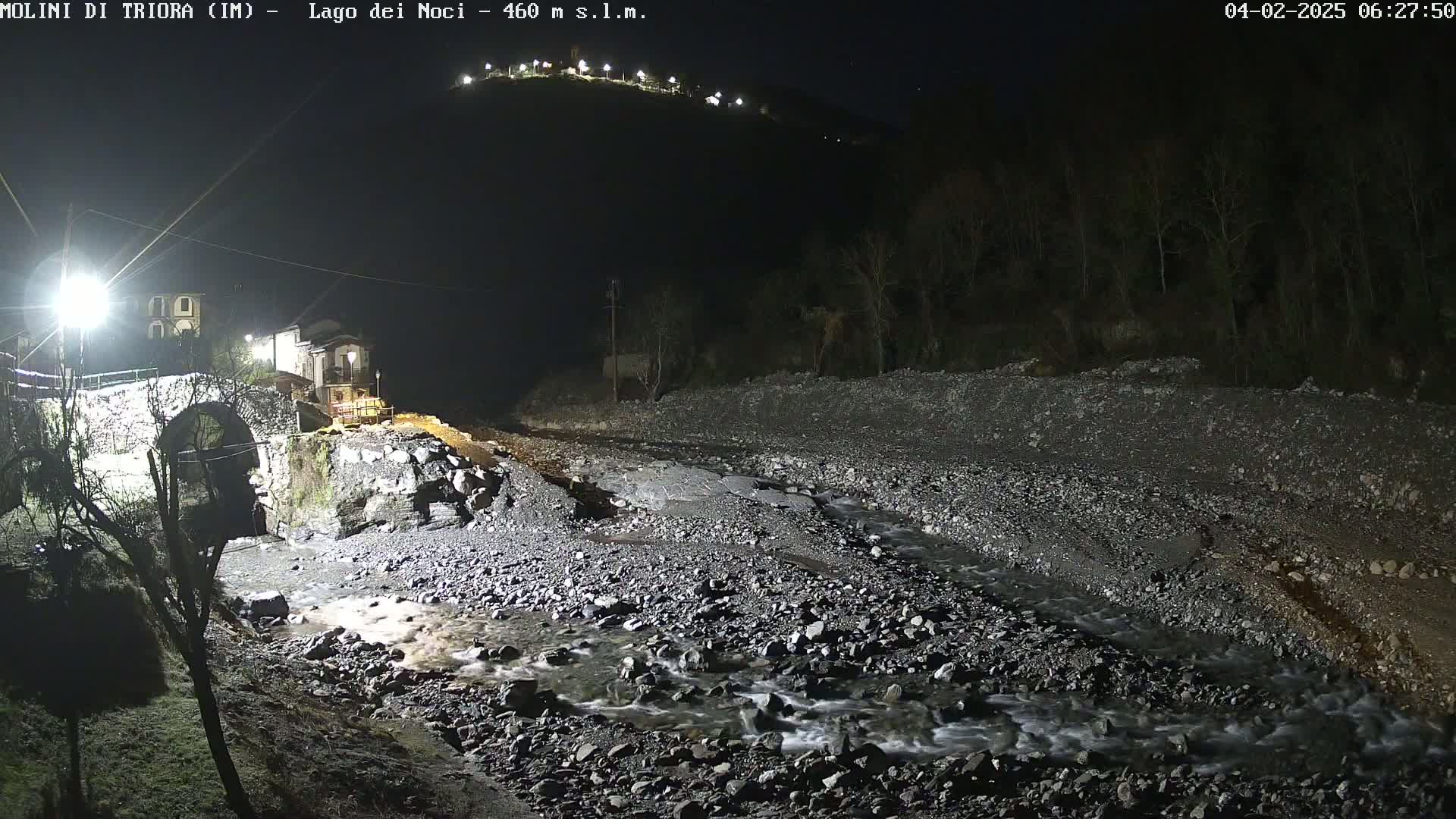A stone bridge is illuminated at night near a rocky streambed under a dark sky.