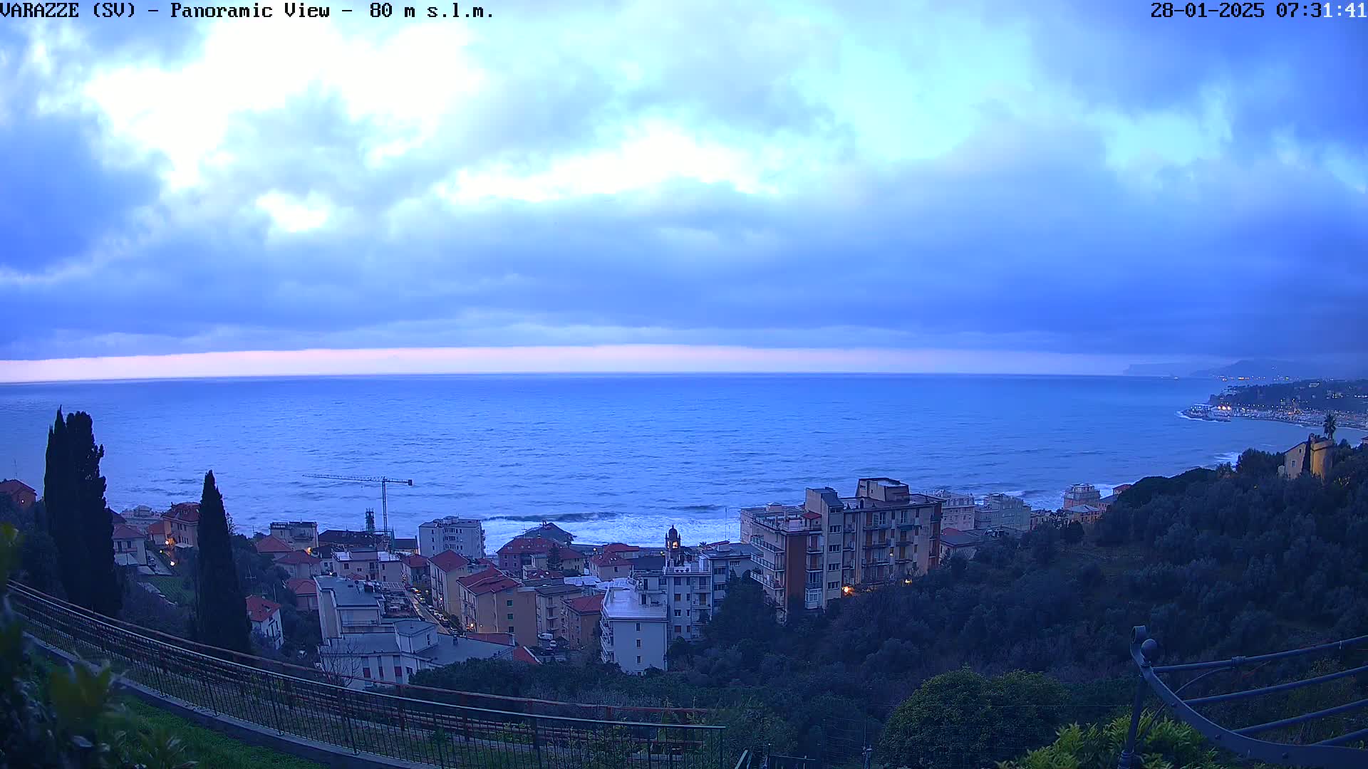A coastal town overlooks a dark blue sea under a mostly cloudy, twilight sky.