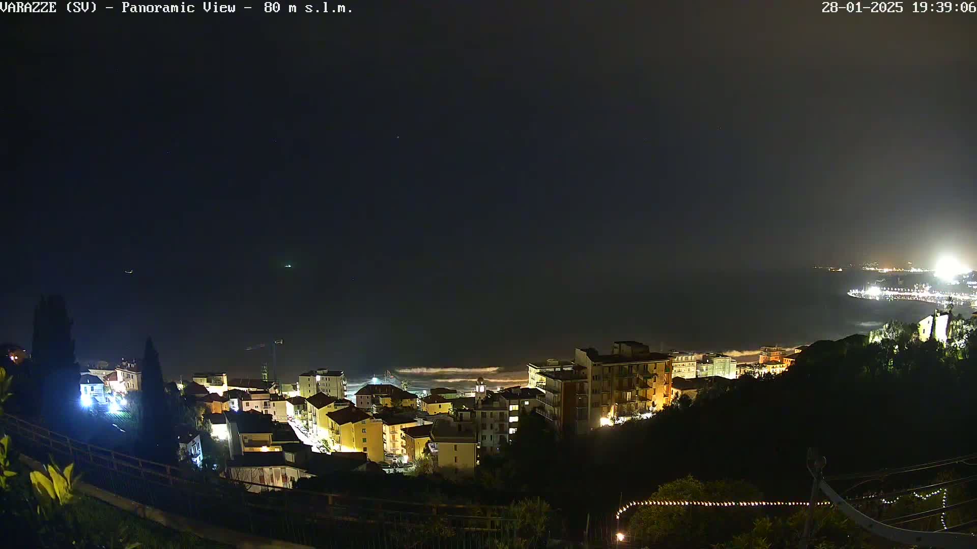 A nighttime panoramic view of a coastal town with its lights illuminated, overlooking a dark ocean under a clear, starlit sky.