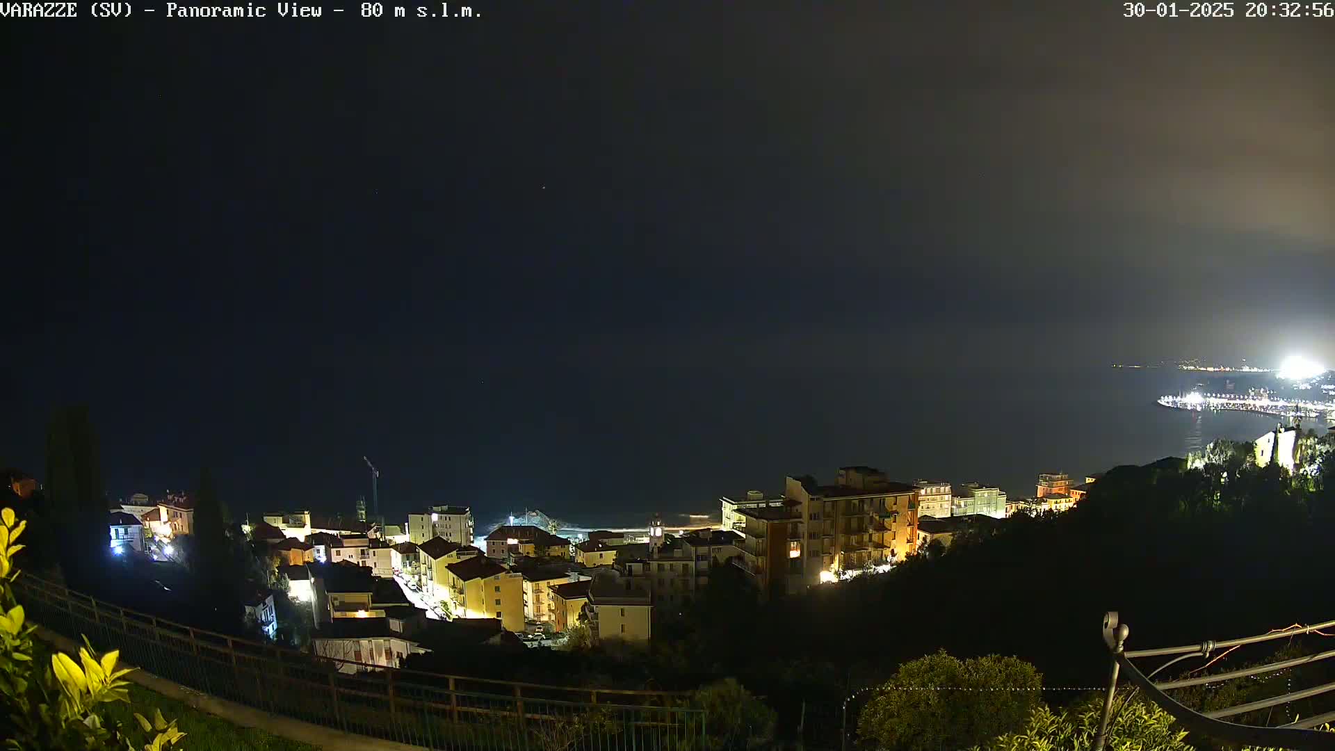A nighttime, panoramic view of a coastal town illuminated with lights, overlooking a dark ocean under a clear sky.