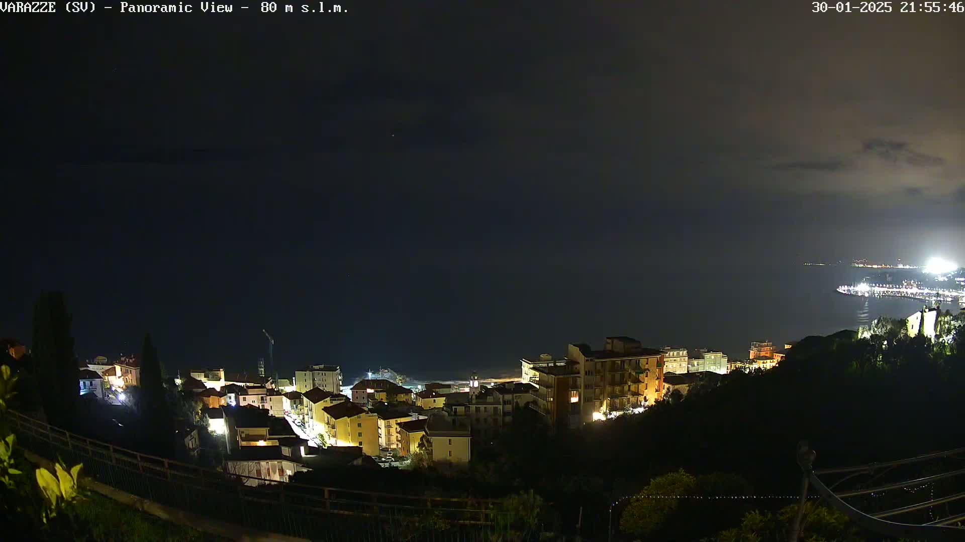 A nighttime panoramic view of a coastal town illuminated with lights, under a dark, cloudy sky.