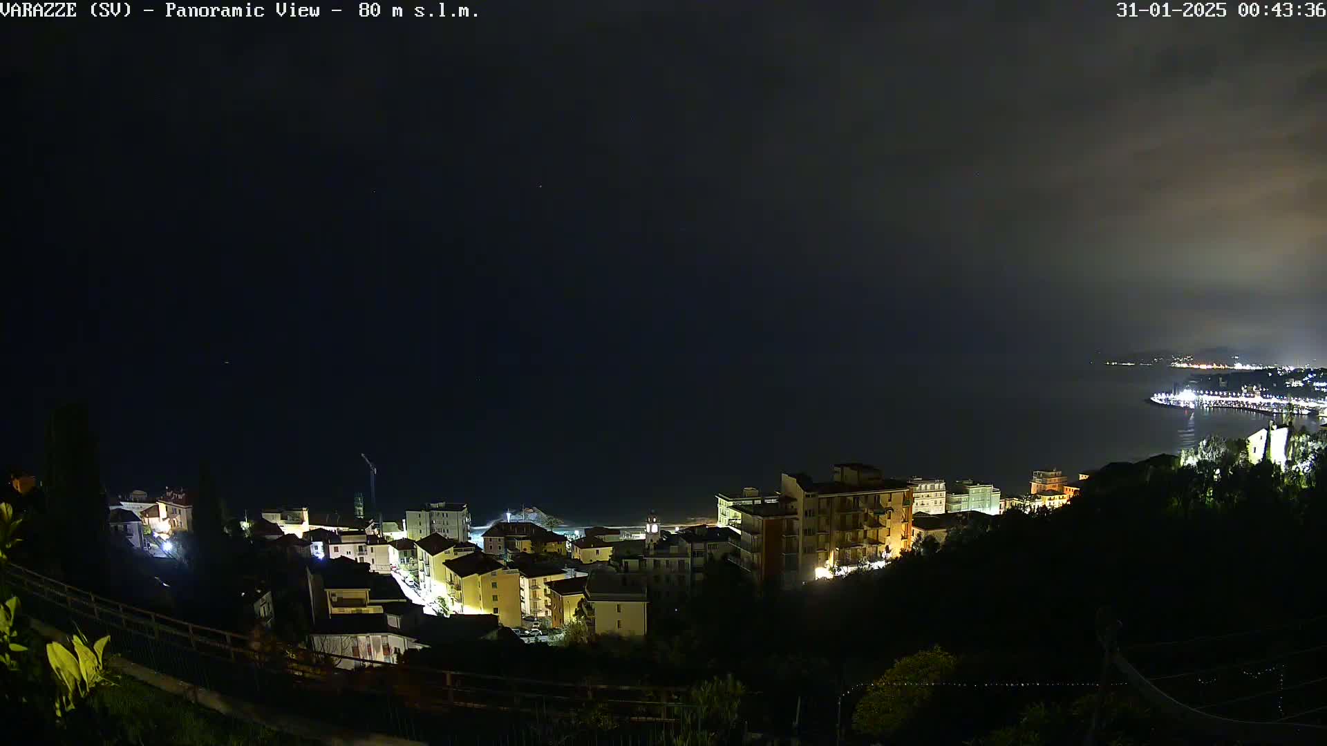 A nighttime, panoramic view of a coastal town with its lights illuminated against a dark sky.