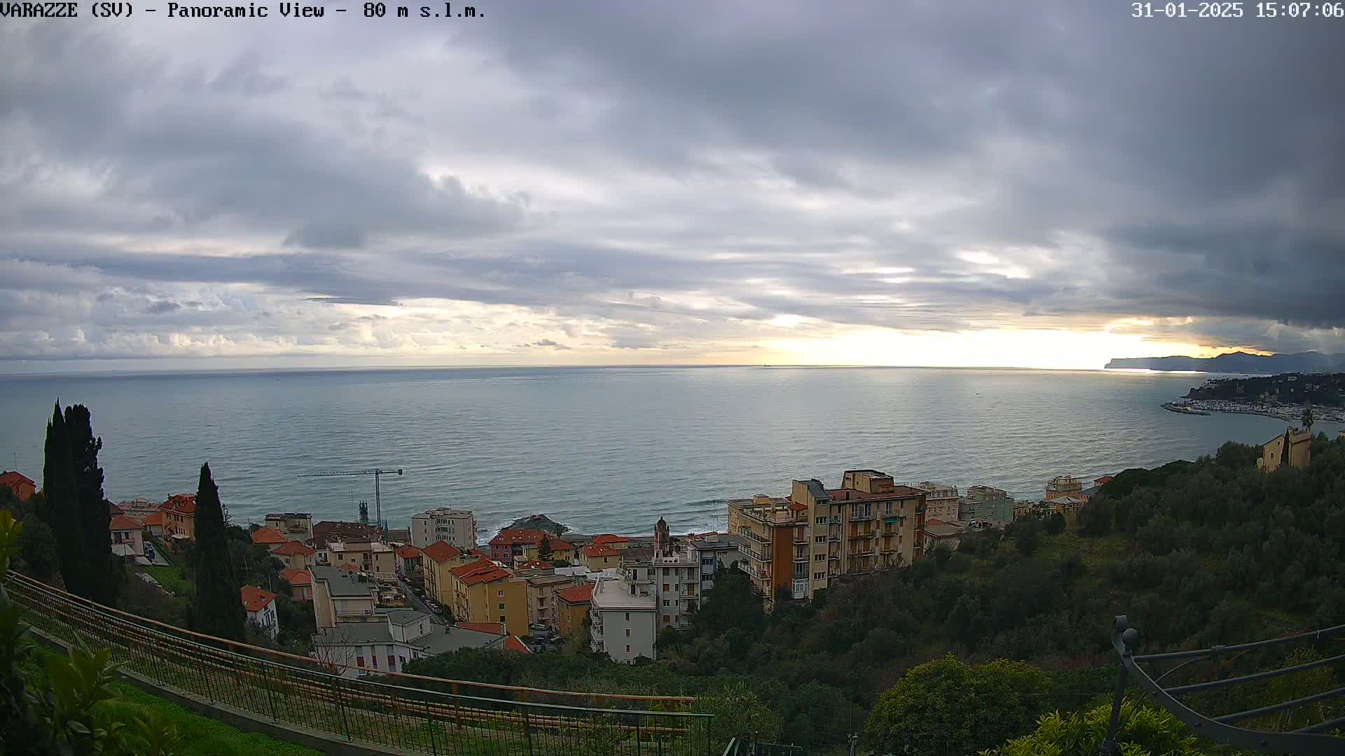 A coastal town overlooks a calm sea under a mostly cloudy sky with a hint of sunset.