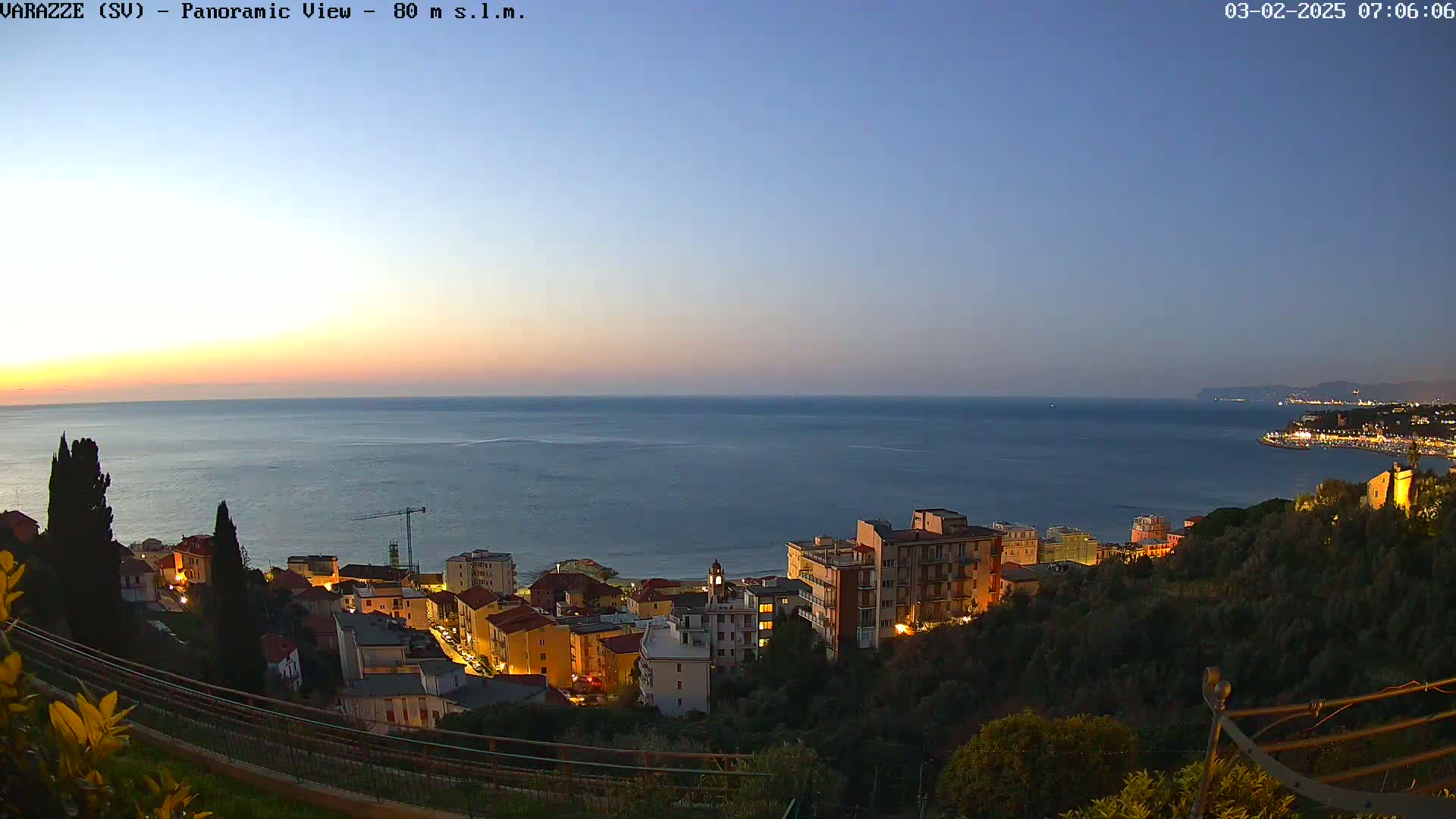 A coastal town with illuminated buildings at twilight overlooks a calm sea under a clear sky.
