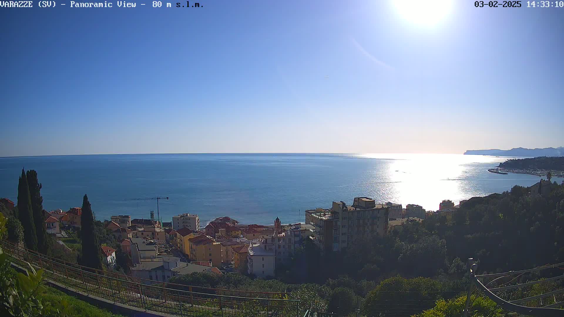 A sunny day overlooking a coastal town and the glistening sea, with a construction crane visible in the distance.