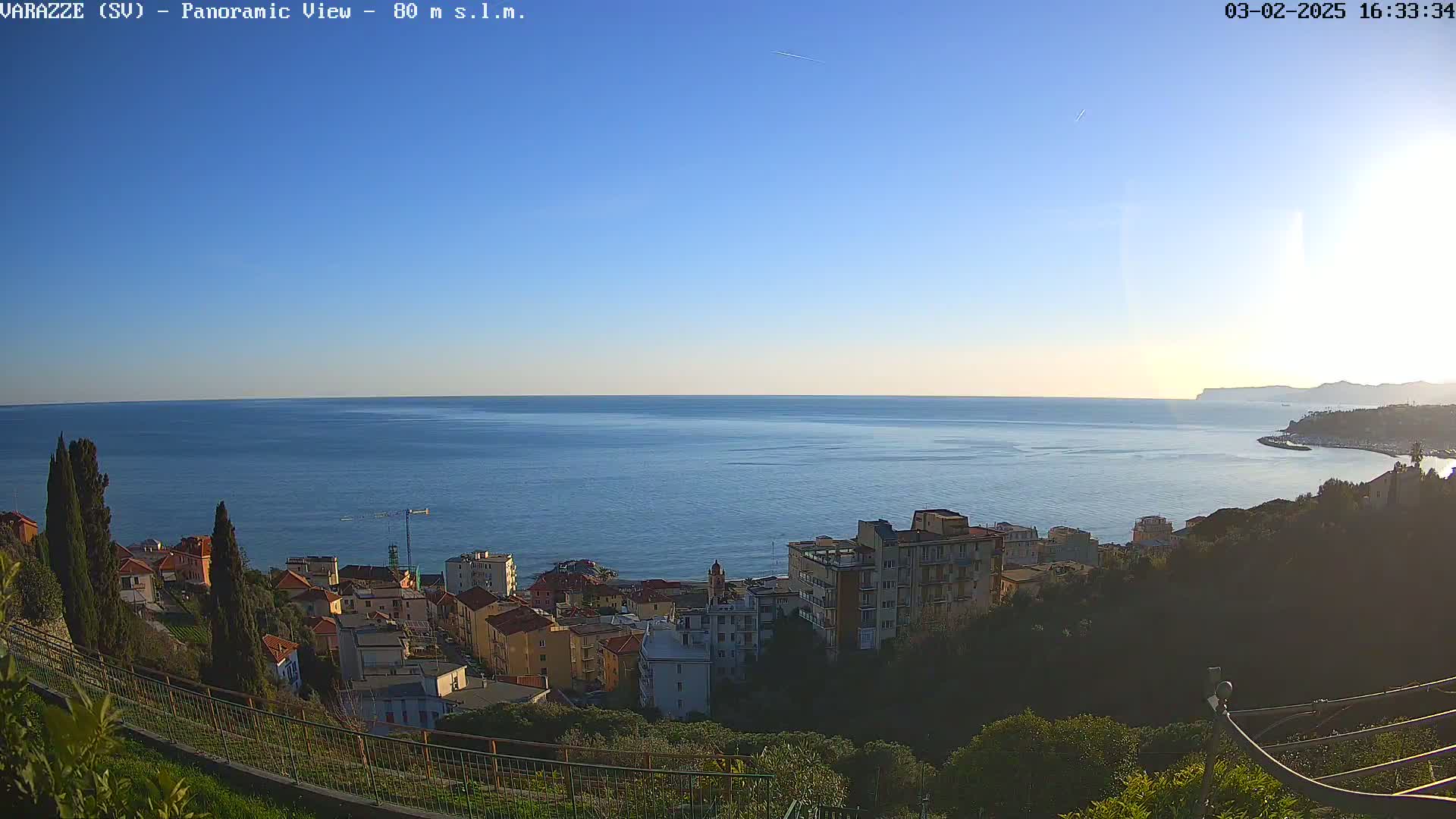 A panoramic view of a coastal town on a clear, sunny day, overlooking a calm sea extending to a distant shoreline.