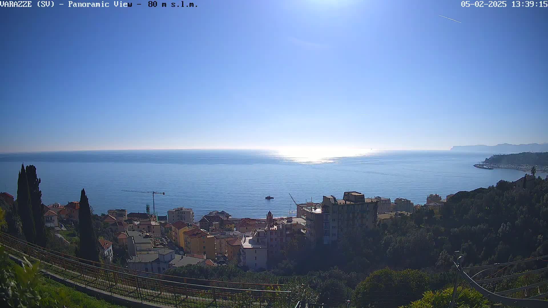 A coastal town nestled on a hillside overlooks a calm, blue sea under a clear, sunny sky.