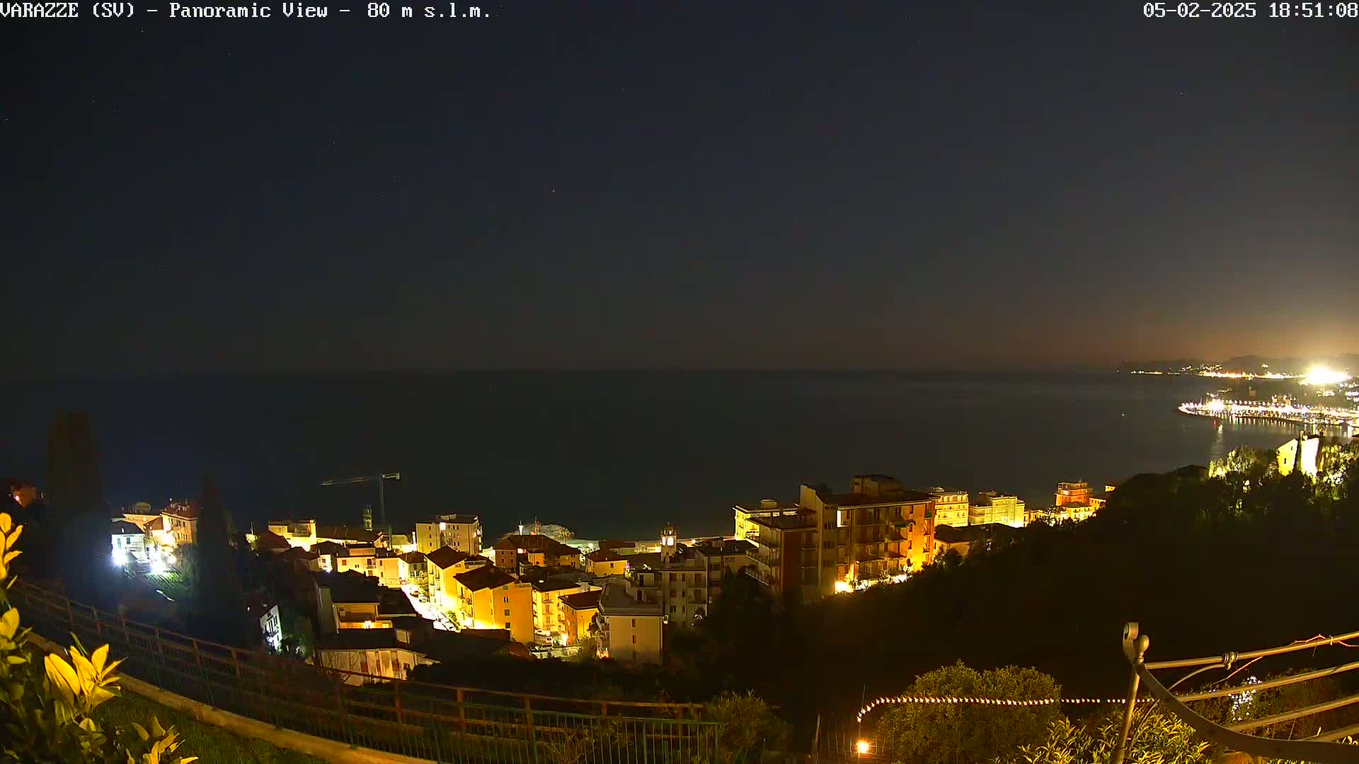 A nighttime panoramic view shows a coastal town illuminated, overlooking a dark sea under a clear, starry sky.