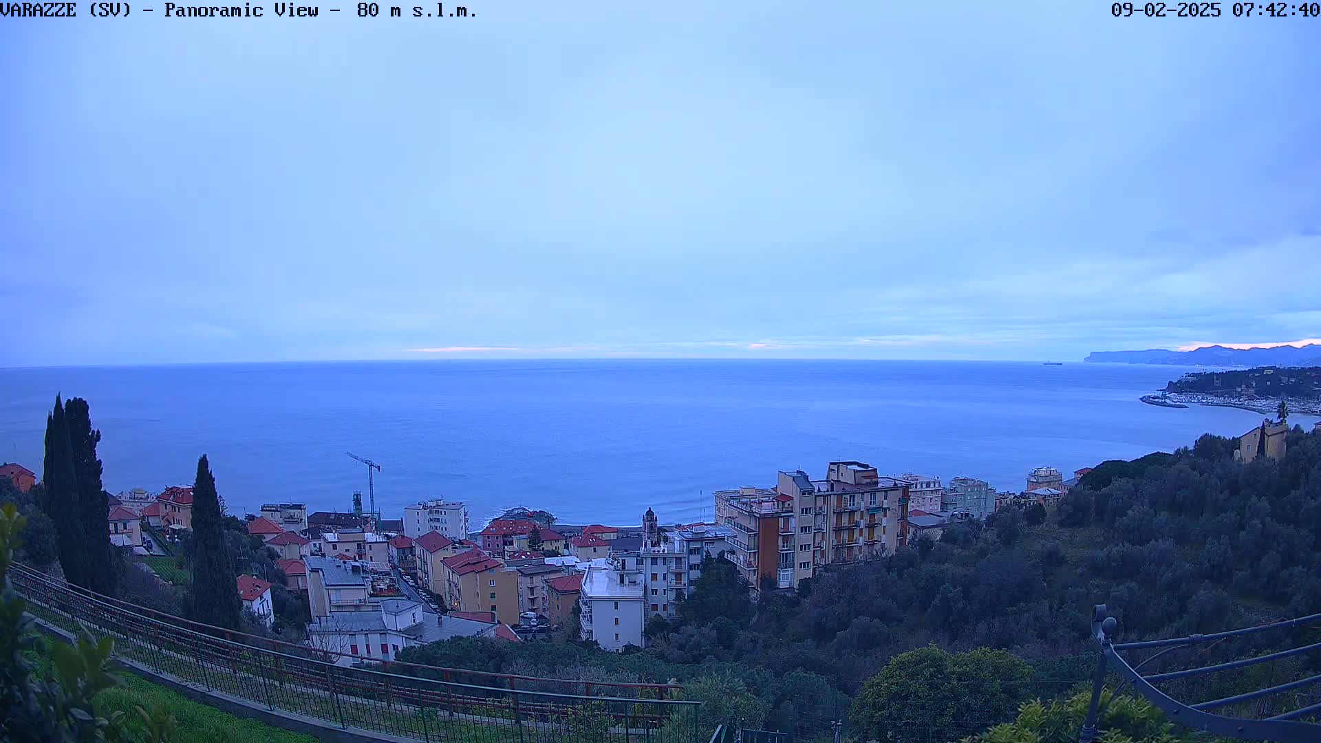 A panoramic view of a coastal town overlooking a calm, blue sea under a clear, twilight sky.