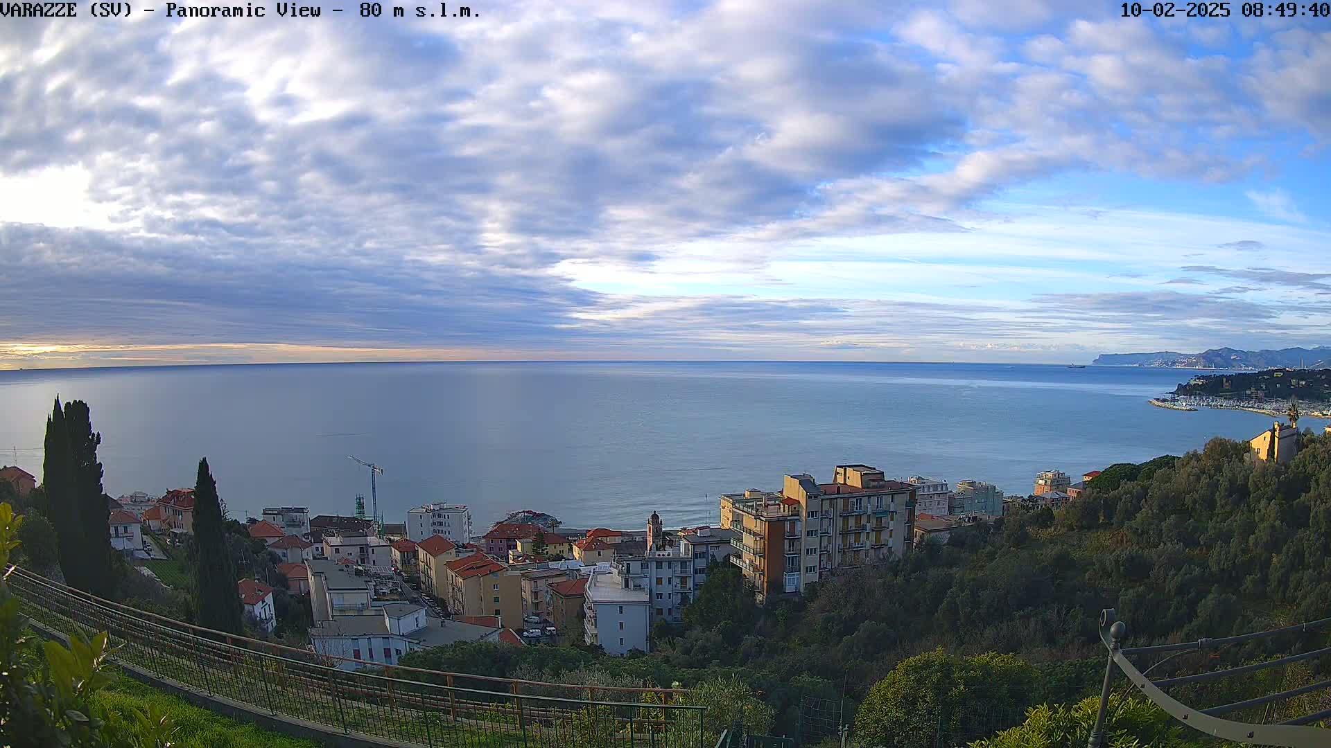 A coastal town nestled on a hillside overlooks a calm sea under a partly cloudy sky.