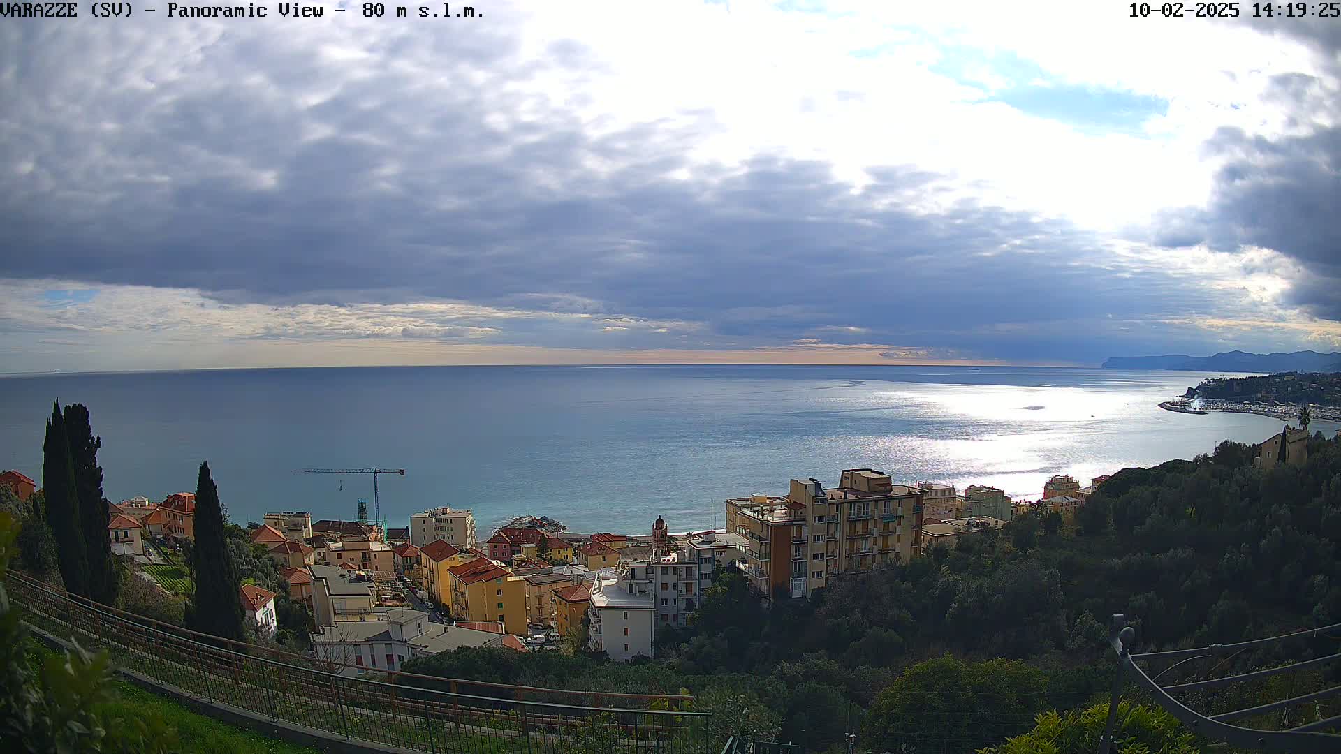 A coastal town nestled on a hillside overlooks a calm sea under a partly cloudy sky.