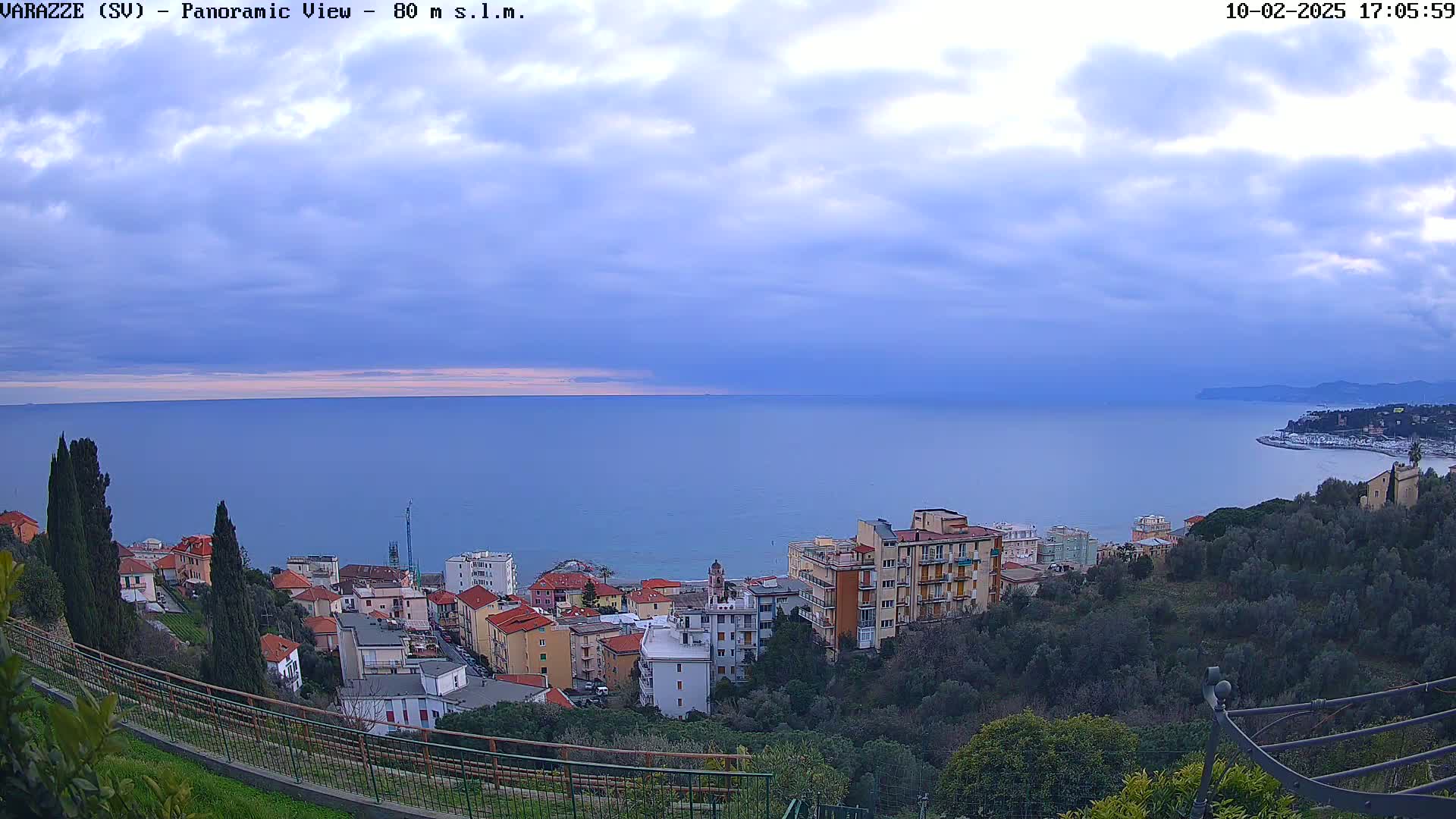 A coastal town with multi-story buildings overlooks a calm sea under a cloudy sky.