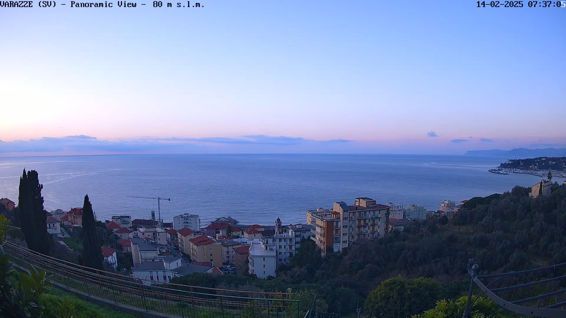 A panoramic view of a coastal town at dawn, overlooking a calm sea under a pale, clear sky.