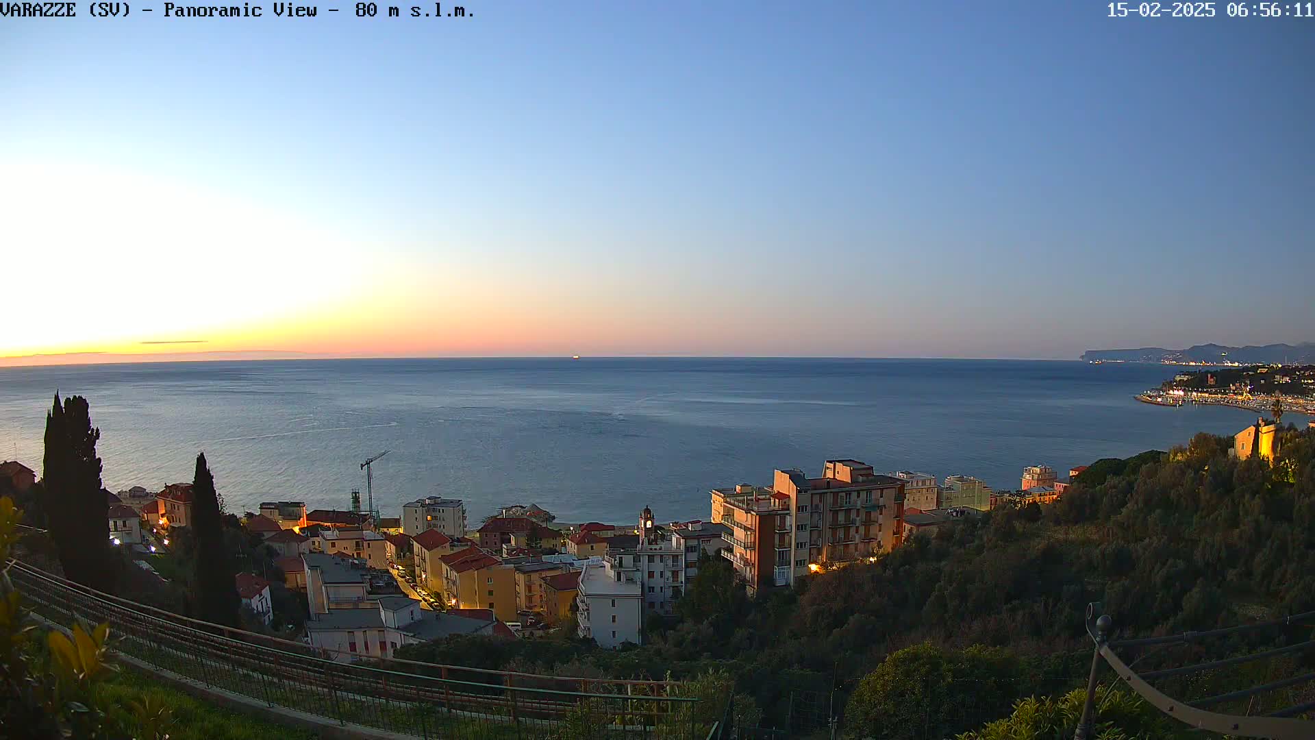 A coastal town at twilight, with buildings illuminated against a calm sea under a clear, sunset sky.
