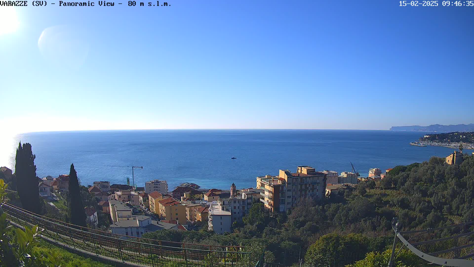 A coastal town with colorful buildings nestled among green trees overlooks a calm blue sea under a clear blue sky.