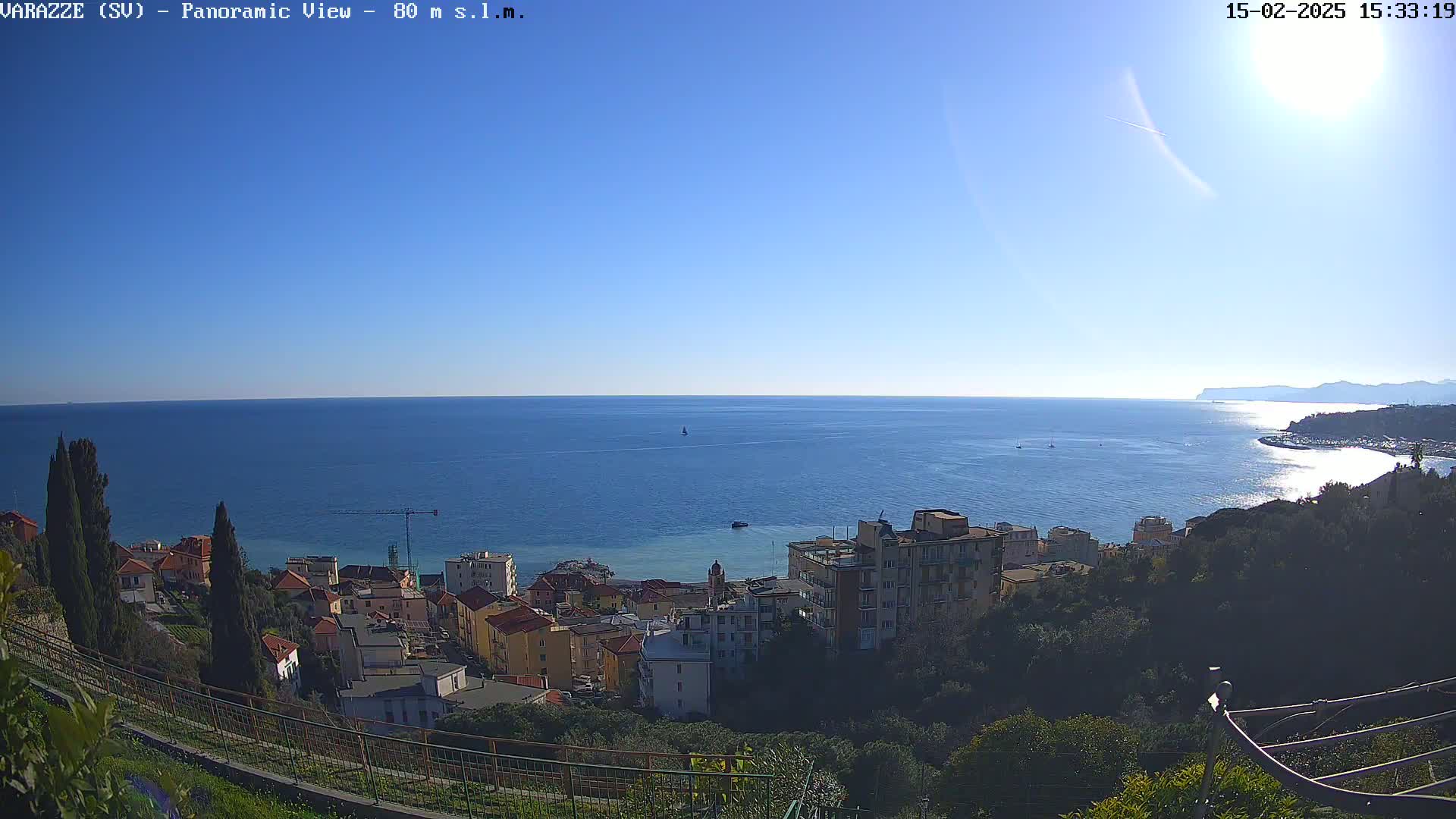 A coastal town nestled on a hillside overlooks a calm, blue sea under a clear, sunny sky.