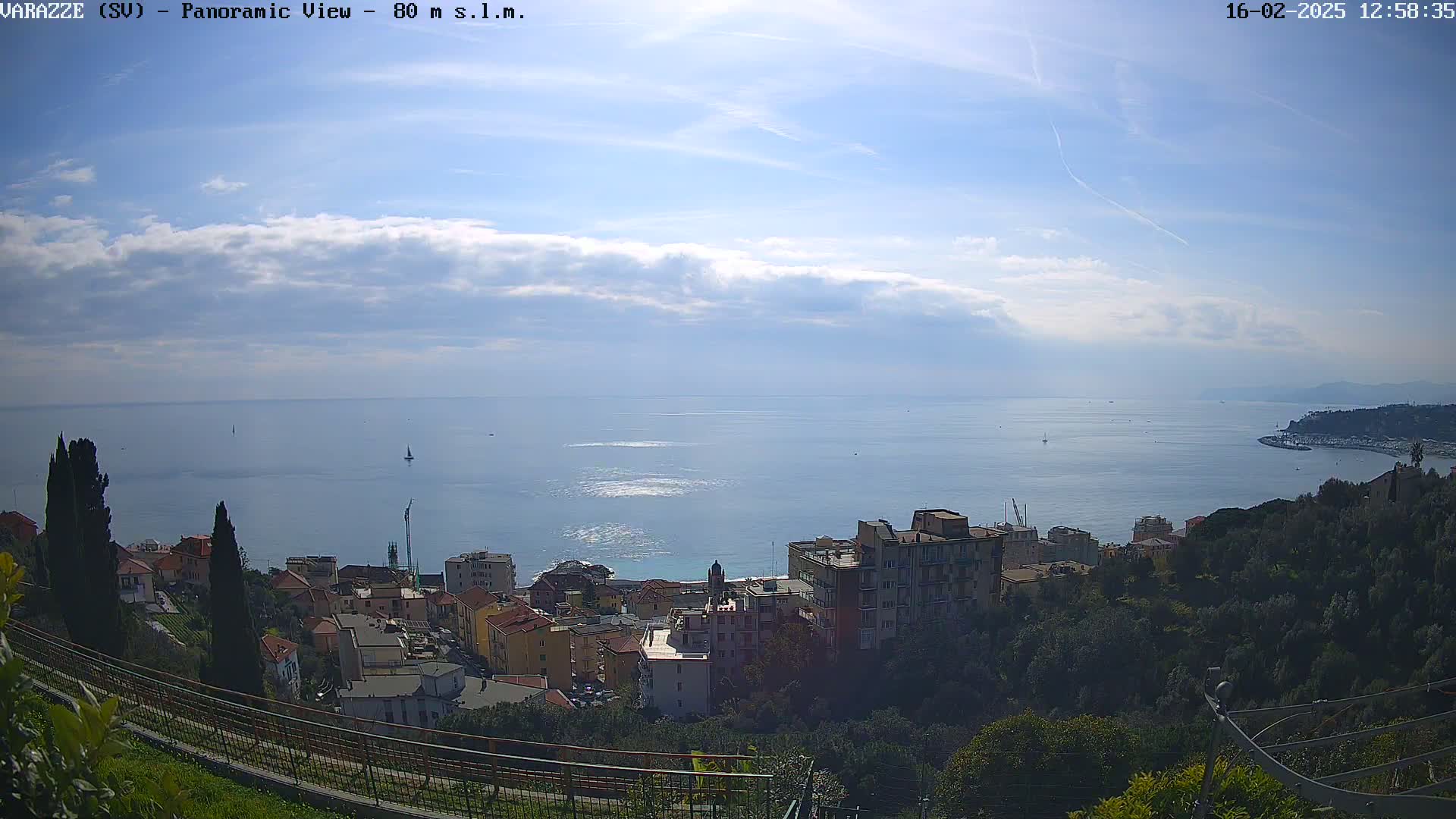 A coastal town nestled on a hillside overlooks a calm sea under a partly cloudy sky.