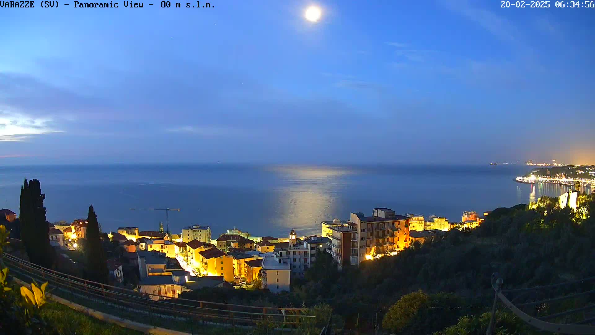 A moonlit coastal town at night, nestled on a hillside overlooking a calm sea under a clear twilight sky.