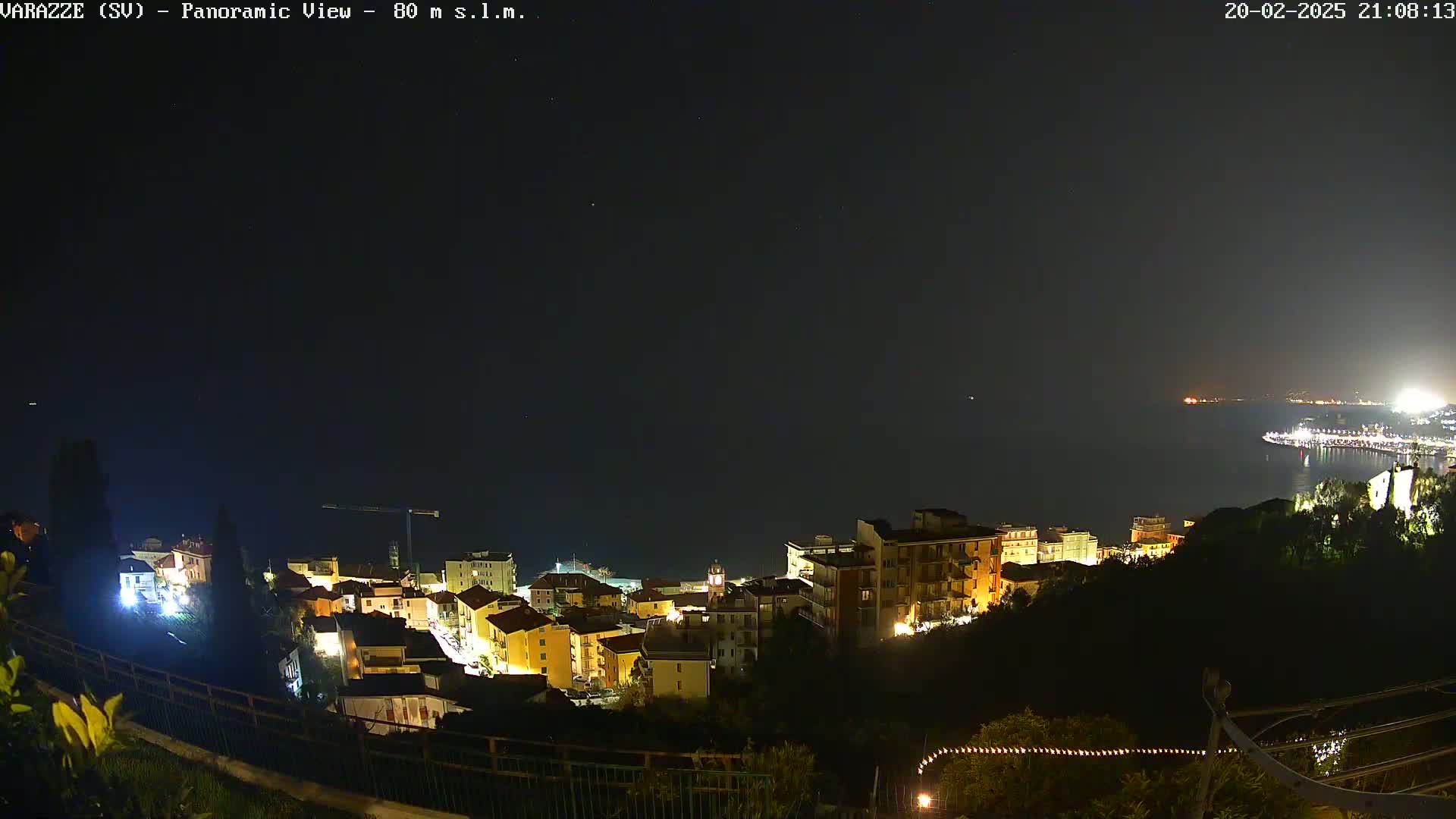 A nighttime panoramic view of a coastal town, with its buildings illuminated, overlooking a dark body of water under a clear, starry sky.