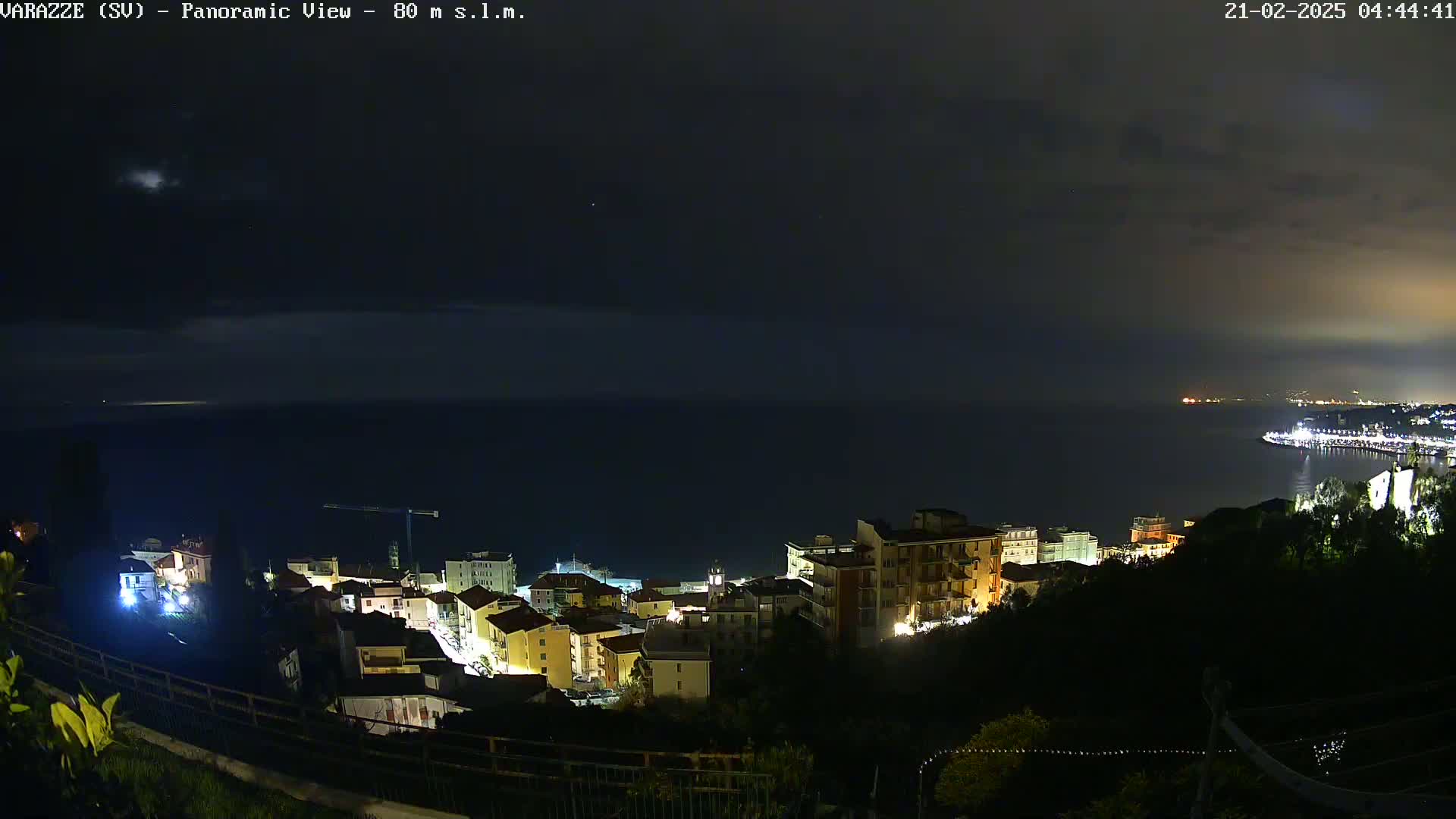 A nighttime panoramic view of a coastal town with its lights illuminated against a dark sea under a mostly clear, dark sky.