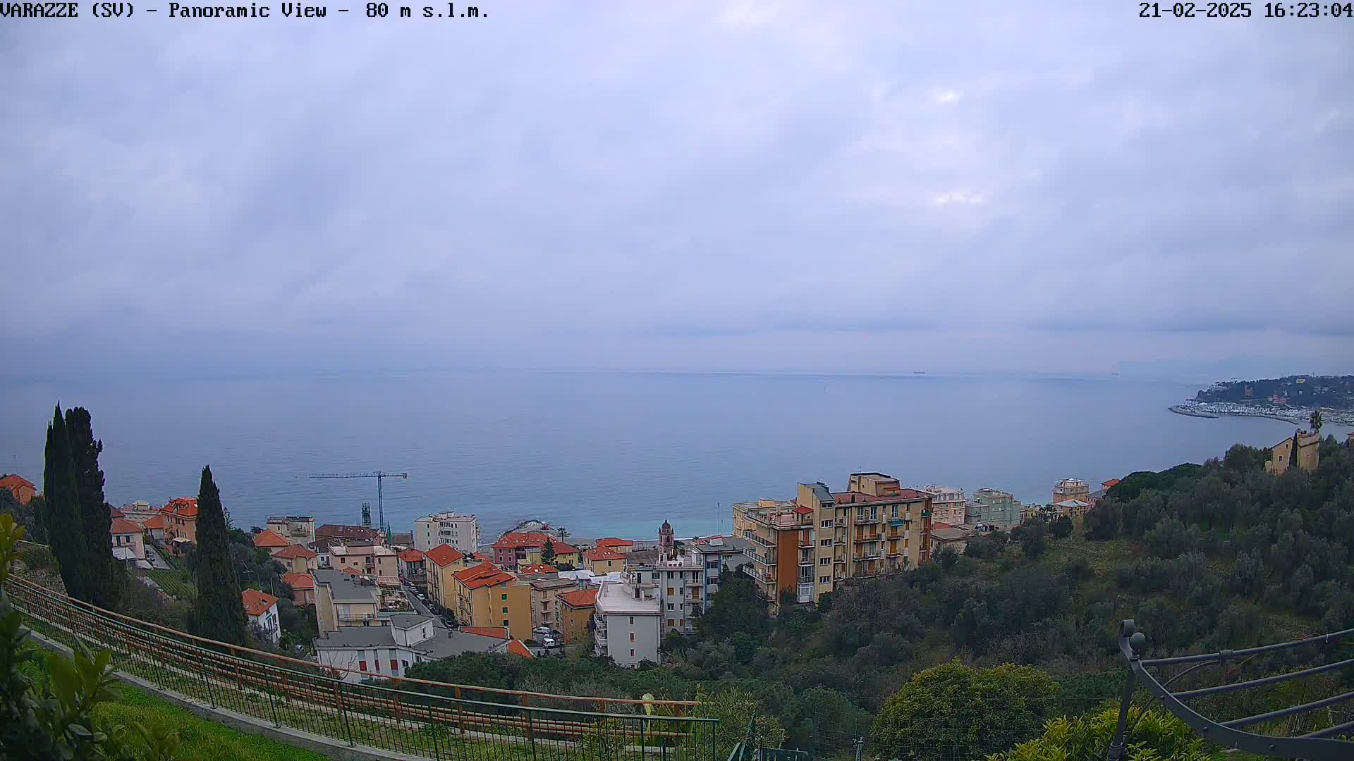 An overcast sky overlooks a coastal town nestled on a hillside overlooking a calm sea.
