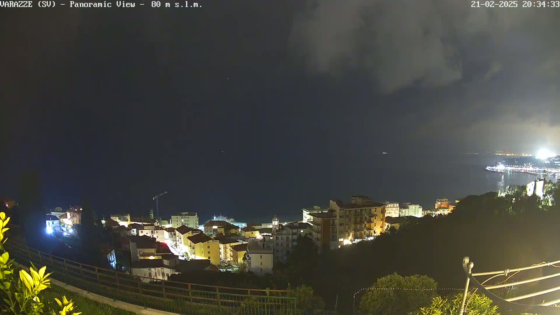 A nighttime panoramic view of a coastal town illuminated with lights under a dark, cloudy sky.