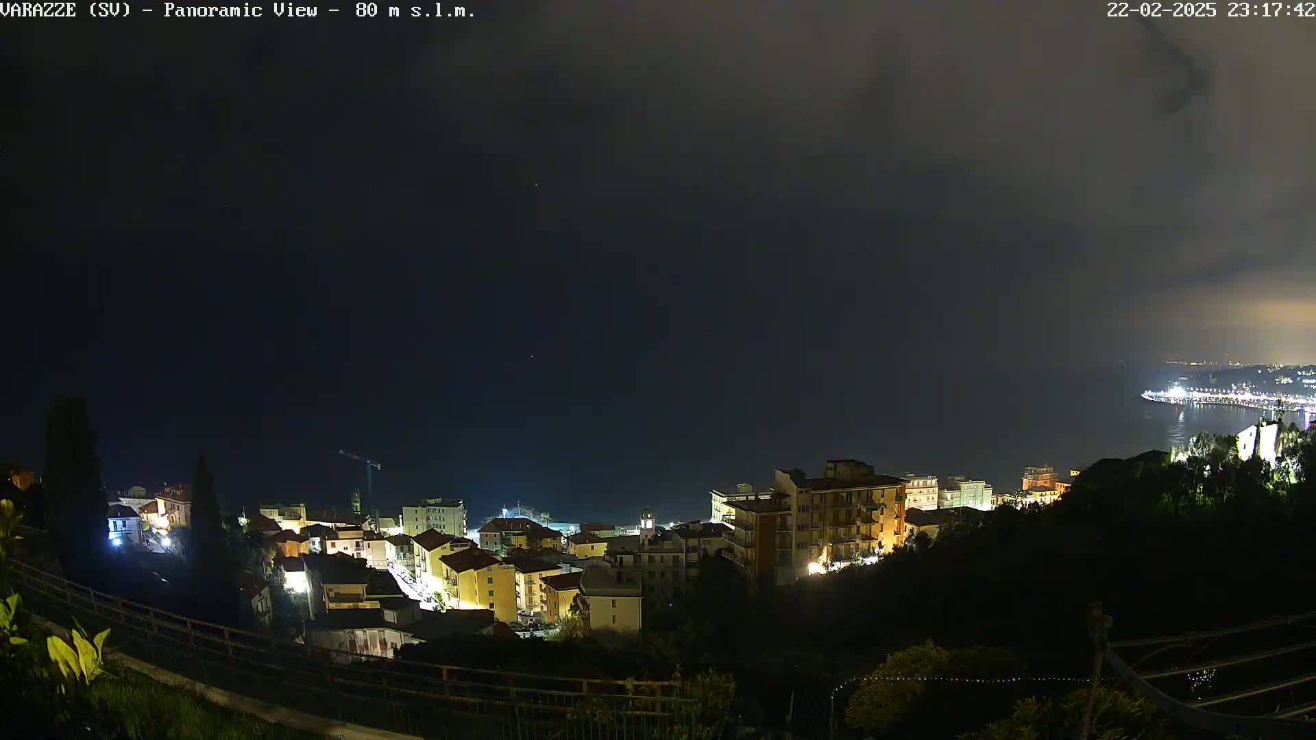 A nighttime, panoramic view of a coastal town illuminated against a dark, cloudy sky.
