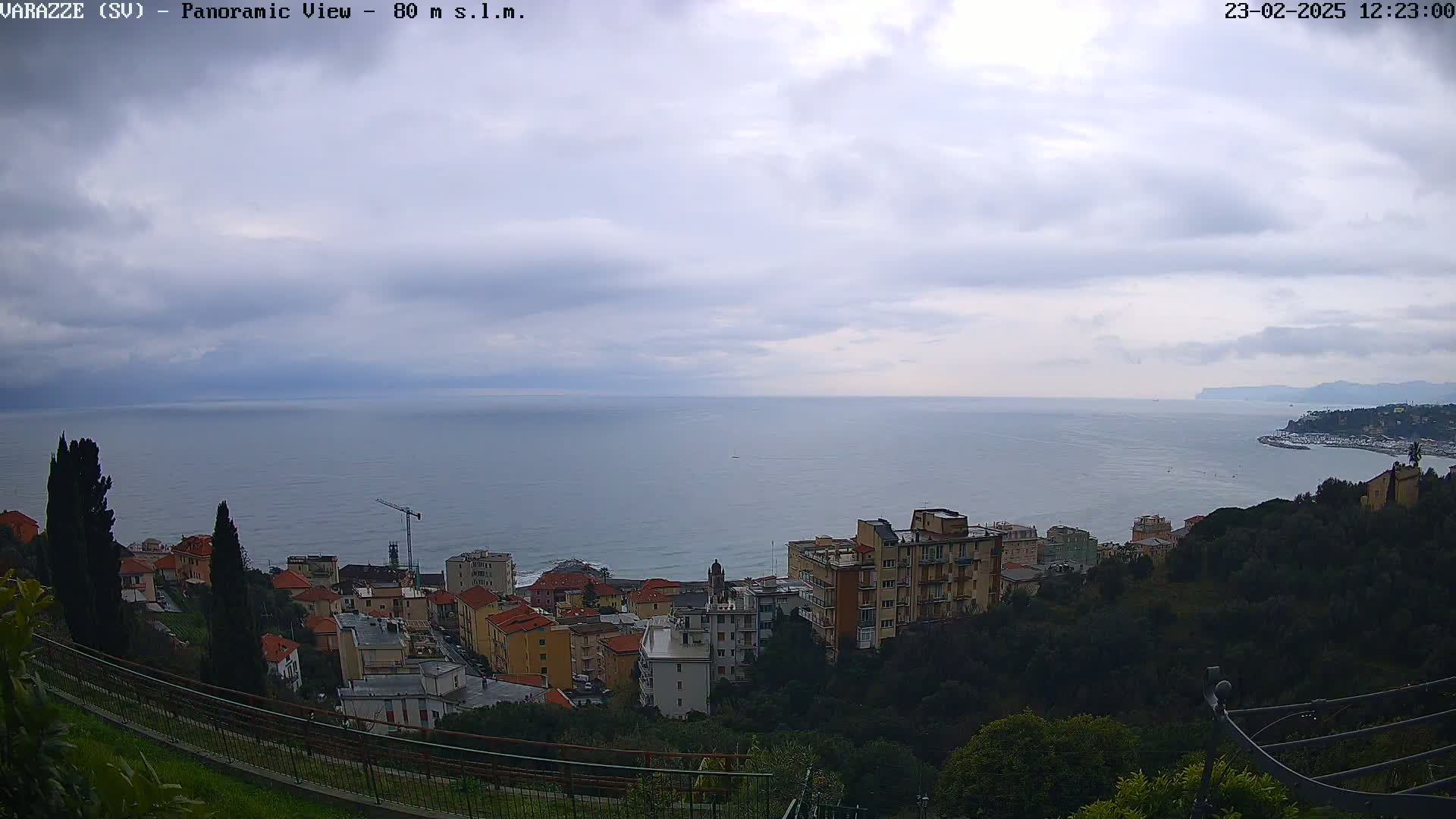An overcast sky overlooks a coastal town with buildings cascading down a hillside towards a calm sea.