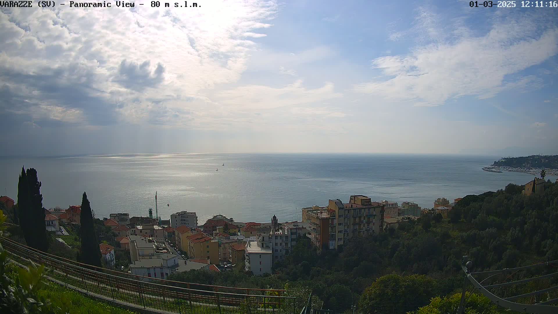 A coastal town nestled on a hillside overlooks a calm sea under a partly cloudy sky.