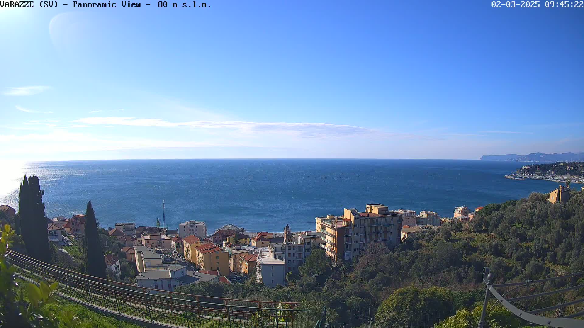 A coastal town nestled on a hillside overlooking a calm blue sea under a clear, sunny sky.
