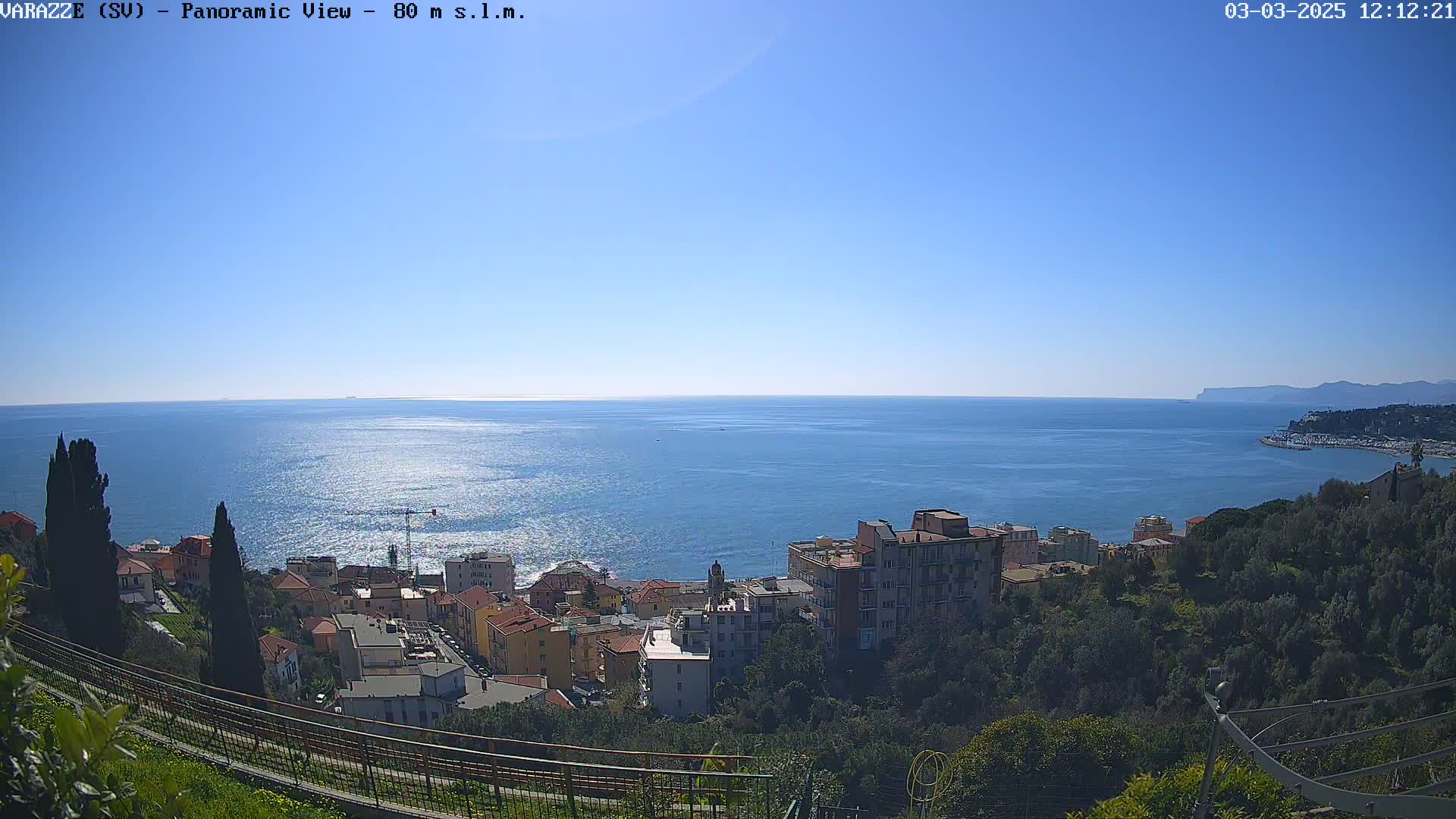 A coastal town nestled on a hillside overlooks a calm, blue sea under a clear sky.