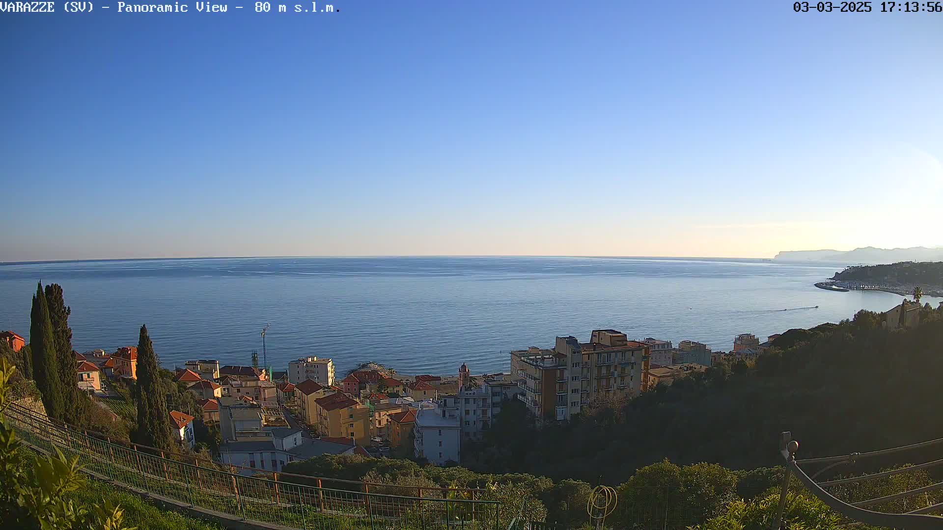 A panoramic view of a coastal town overlooking a calm sea under a clear blue sky.