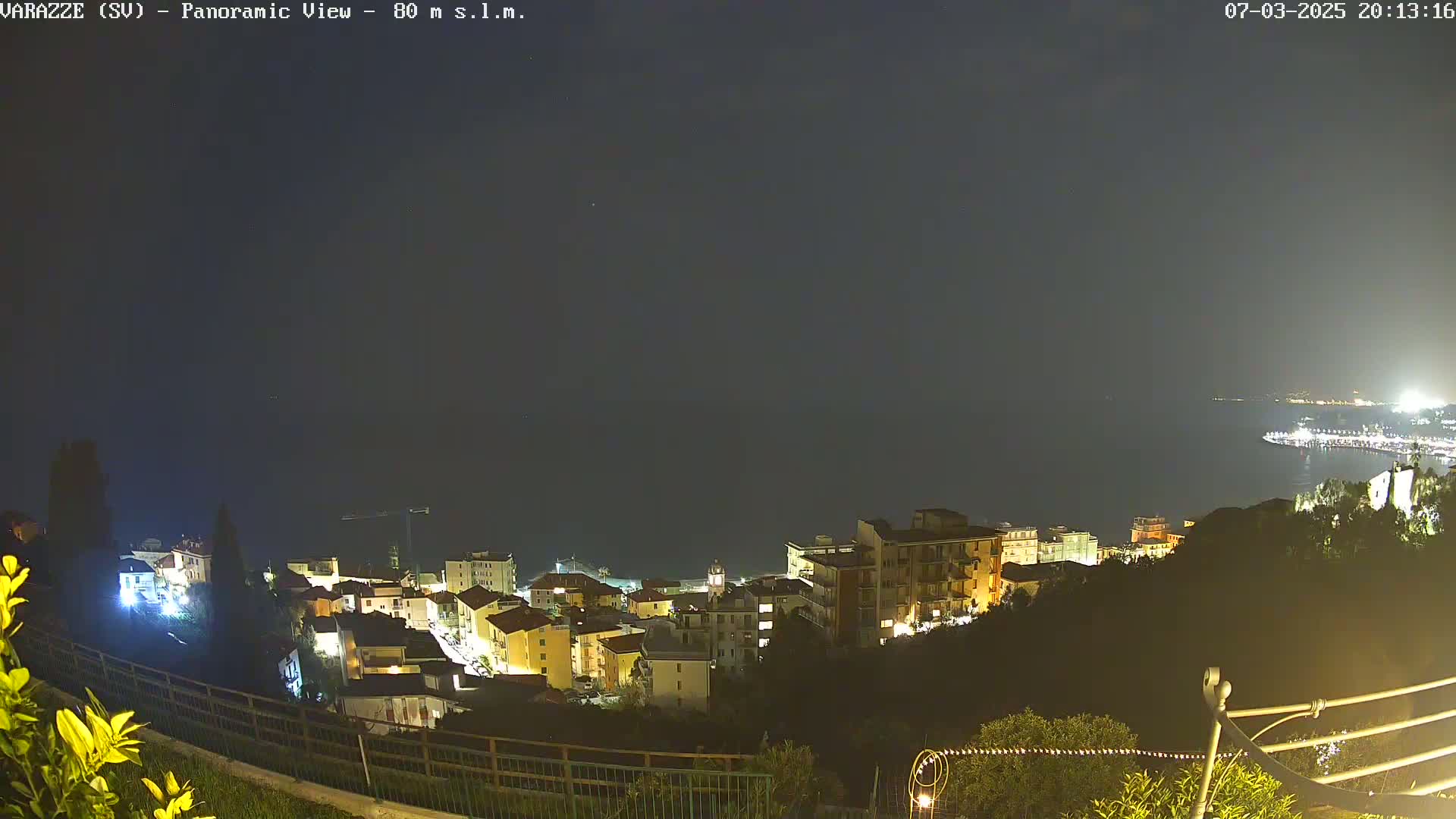 A nighttime, panoramic view of a coastal town illuminated, overlooking a dark sea under a clear sky.