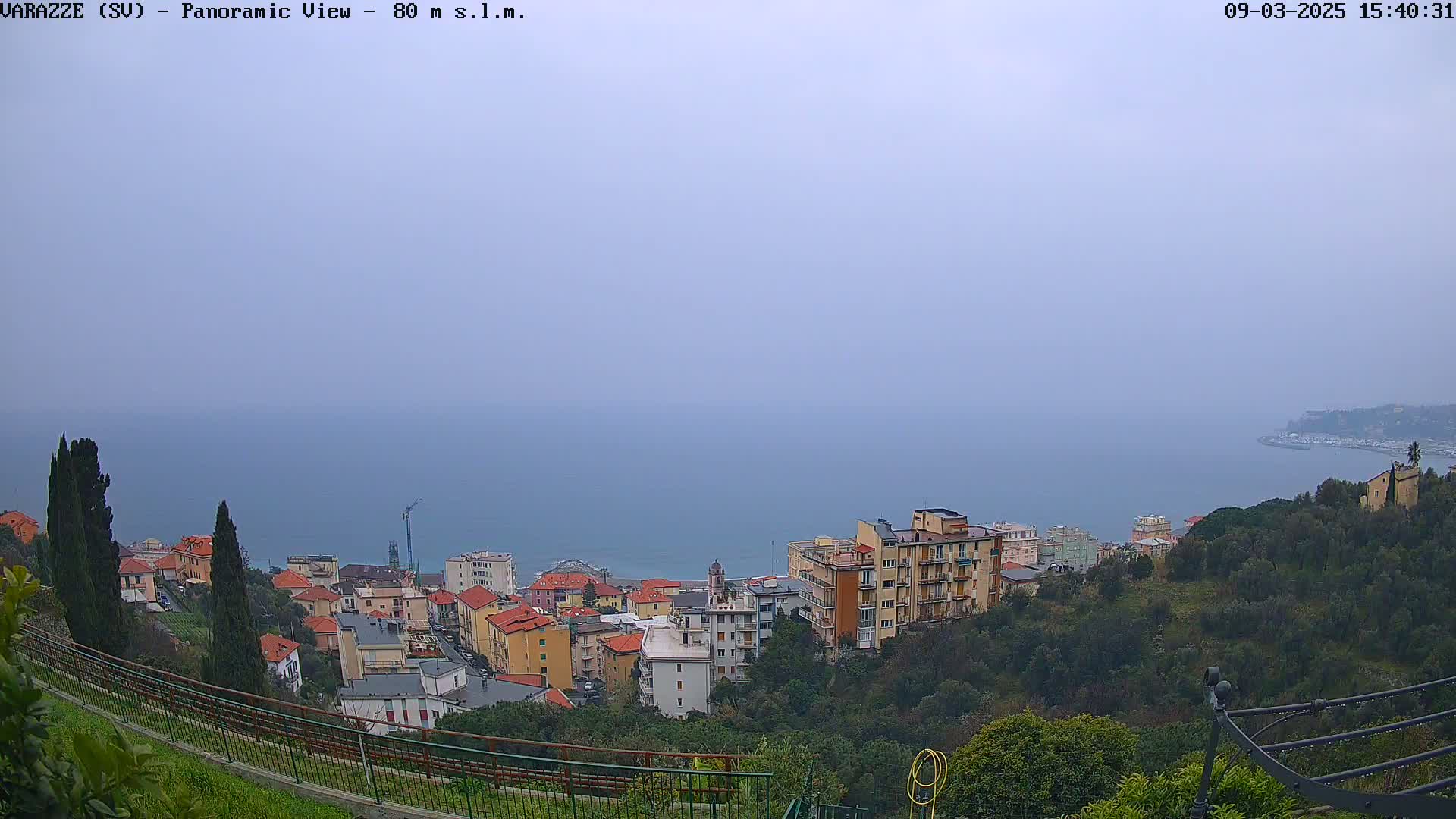 A hazy view overlooking a coastal town with buildings cascading down a hillside towards a calm sea.