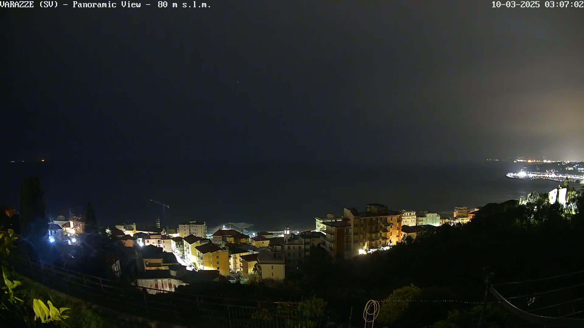 A nighttime, slightly hazy view shows a coastal town with its lights illuminated against a dark ocean.