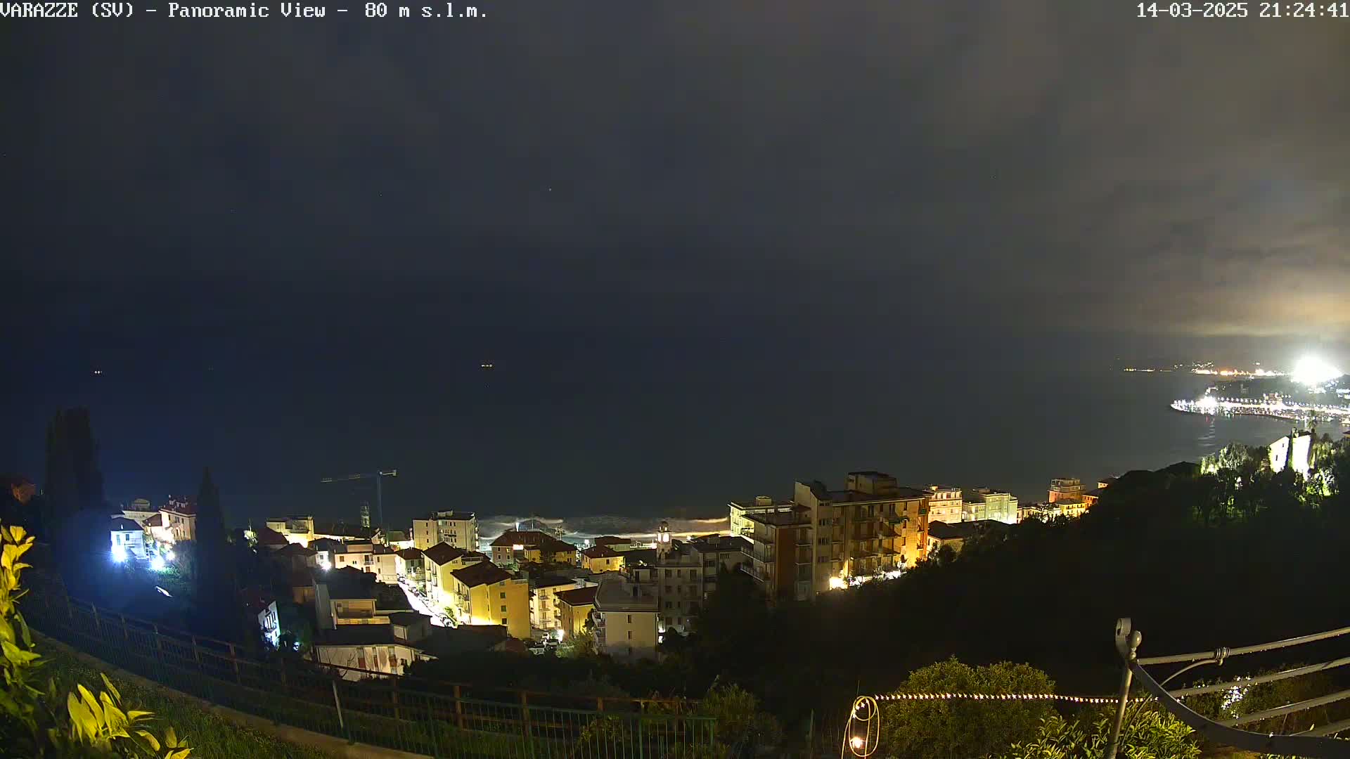 A nighttime panoramic view shows a coastal town with illuminated buildings overlooking a dark sea under a mostly clear sky.