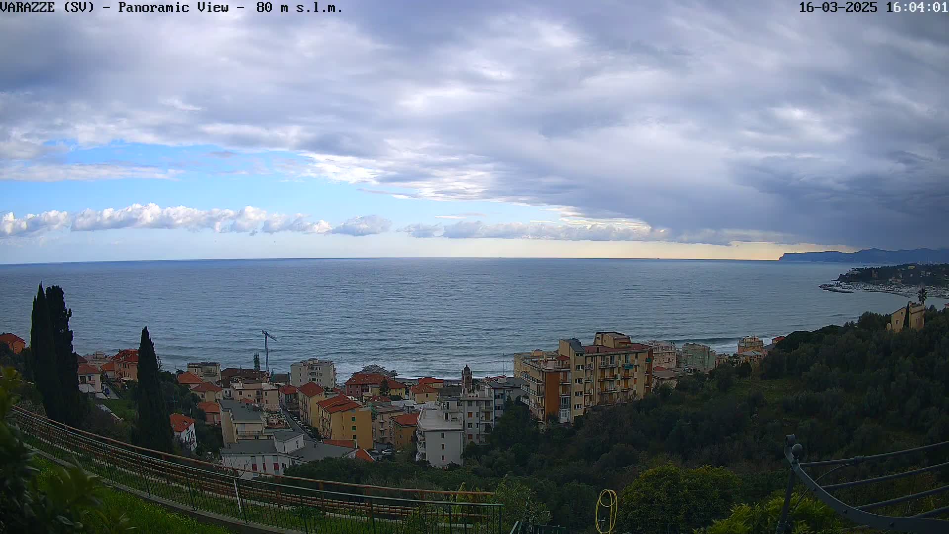 A panoramic view of a coastal town overlooking a calm sea under a partly cloudy sky.