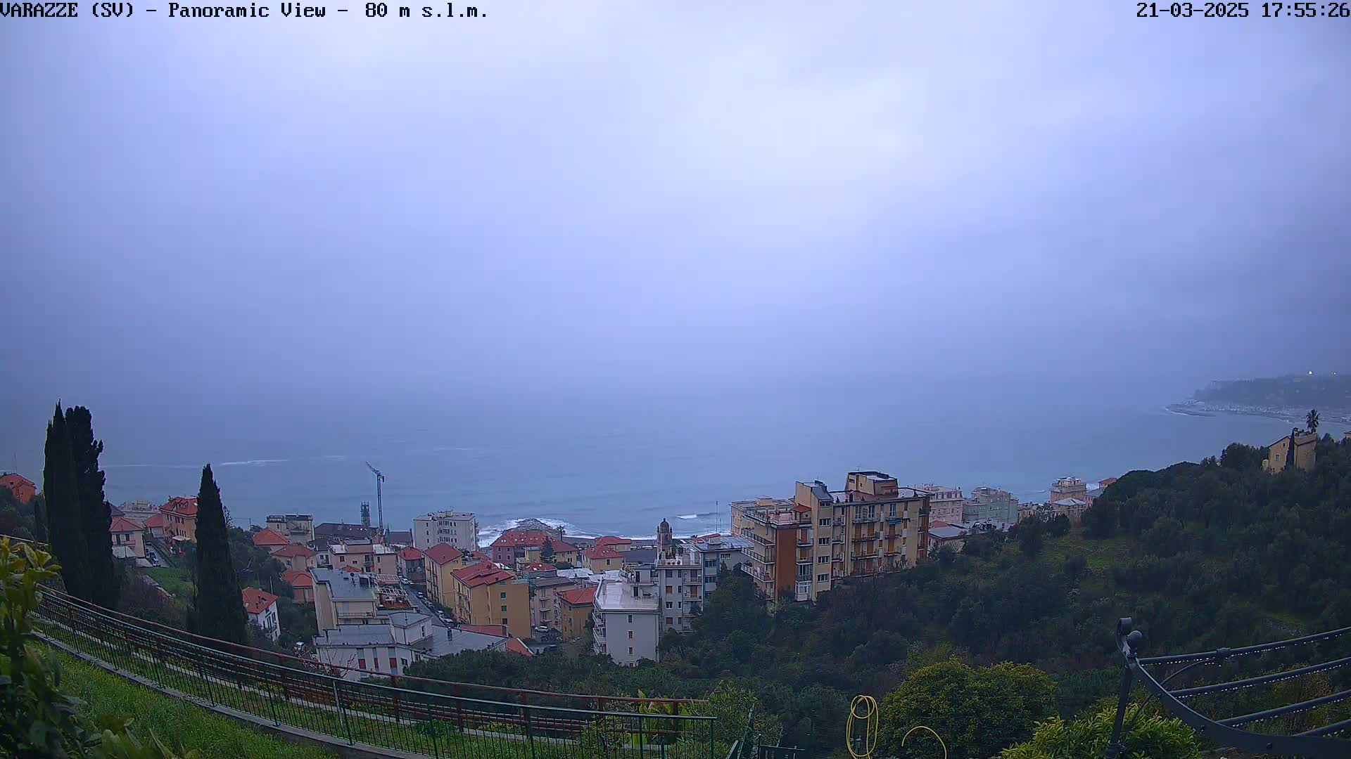 A hazy, overcast view of a coastal town situated on a hillside overlooking a calm sea.