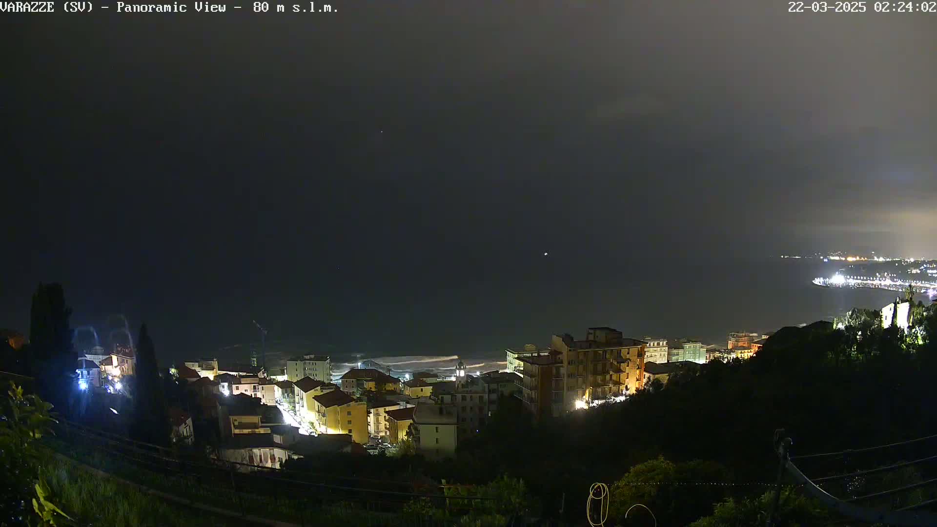 A nighttime, panoramic view of a coastal town illuminated with lights under a dark, overcast sky.