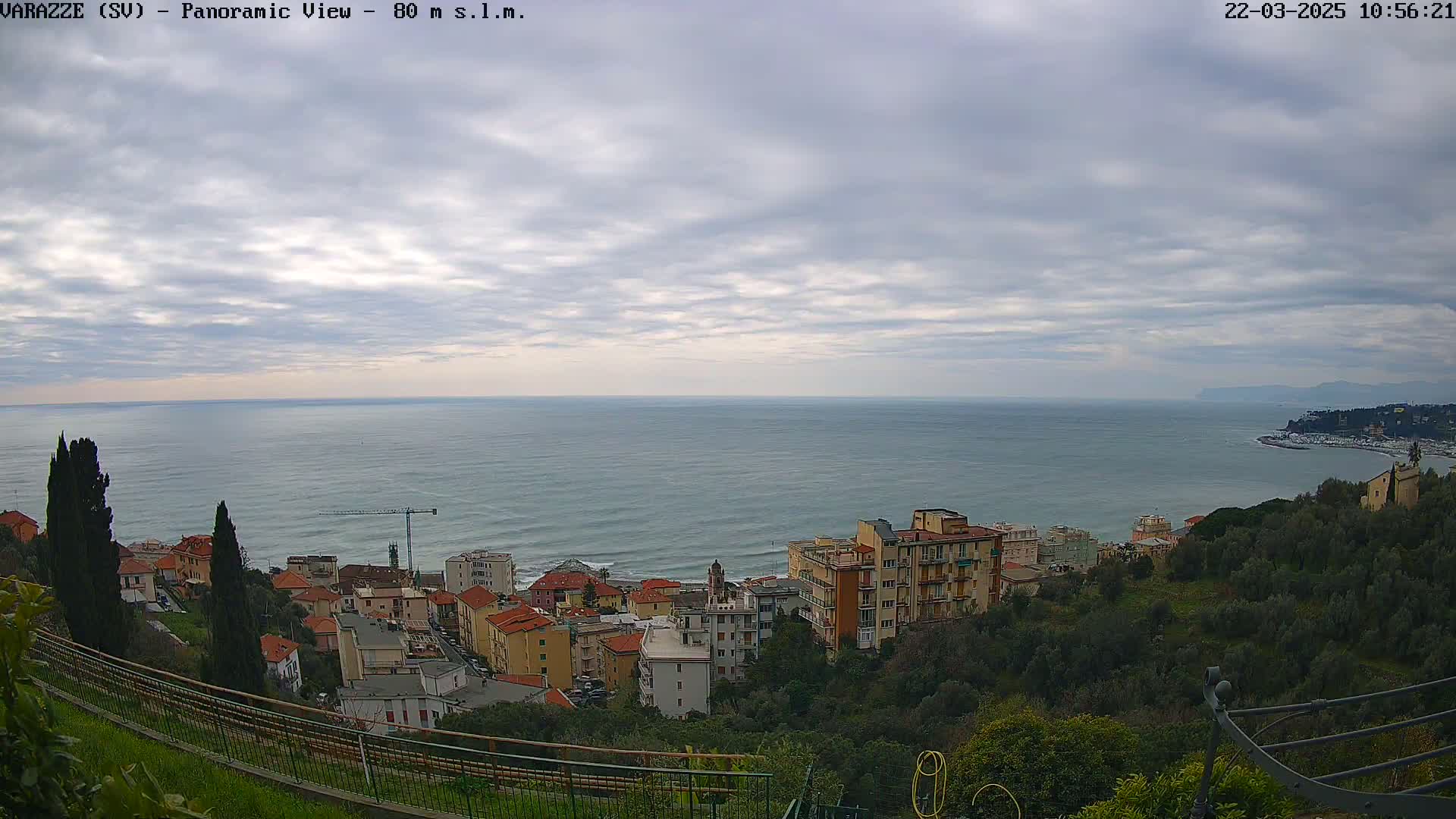 A coastal town nestled on a hillside overlooks a calm sea under a cloudy sky.