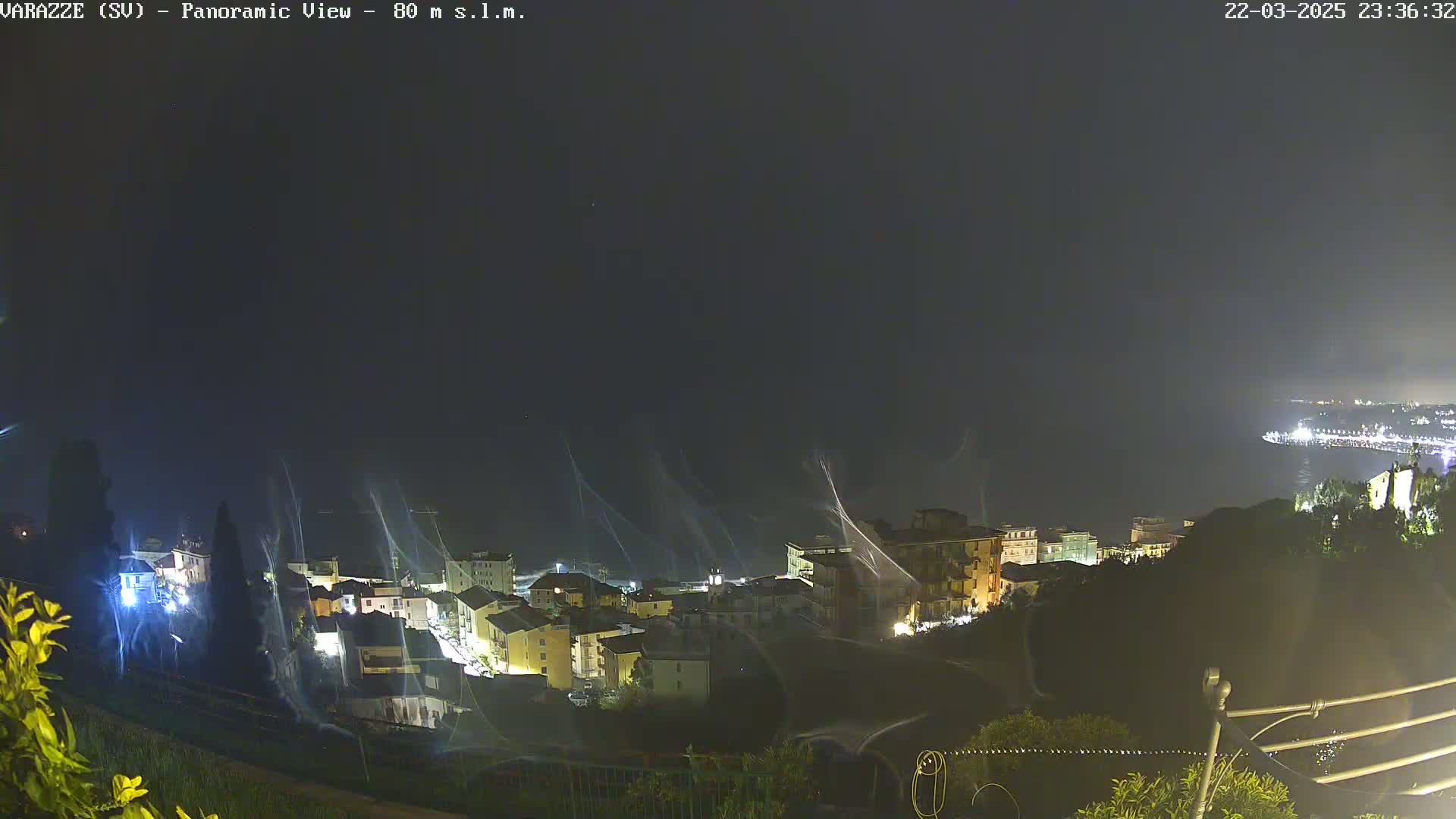 A nighttime panoramic view of a coastal town with illuminated buildings, under a dark, windy sky.