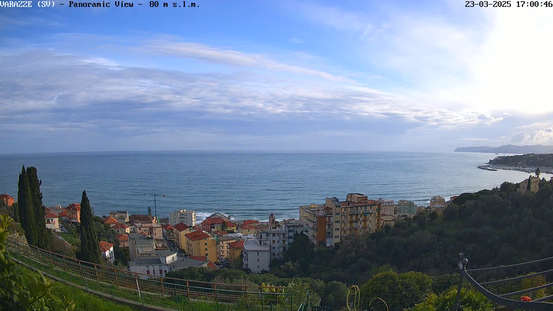 A panoramic view of a coastal town under a partly cloudy sky, with the ocean extending to the horizon.