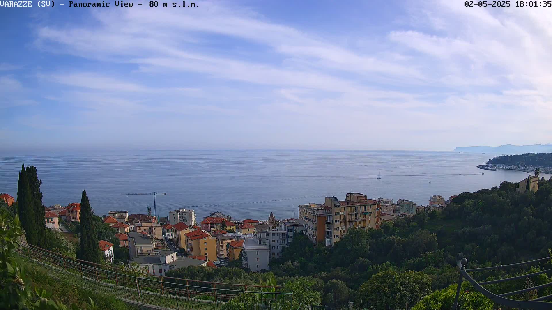 A panoramic view of a coastal town nestled on a hillside overlooking a calm sea under a partly cloudy sky.