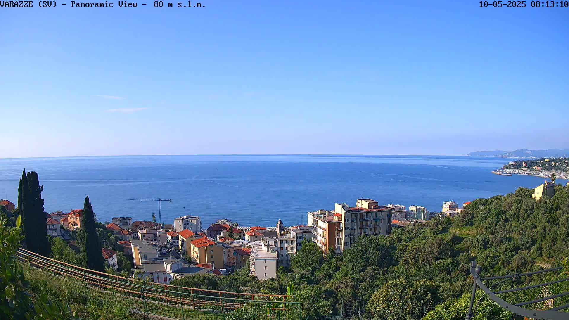 A seaside town nestled on a hillside overlooks a calm, blue sea under a clear sky.