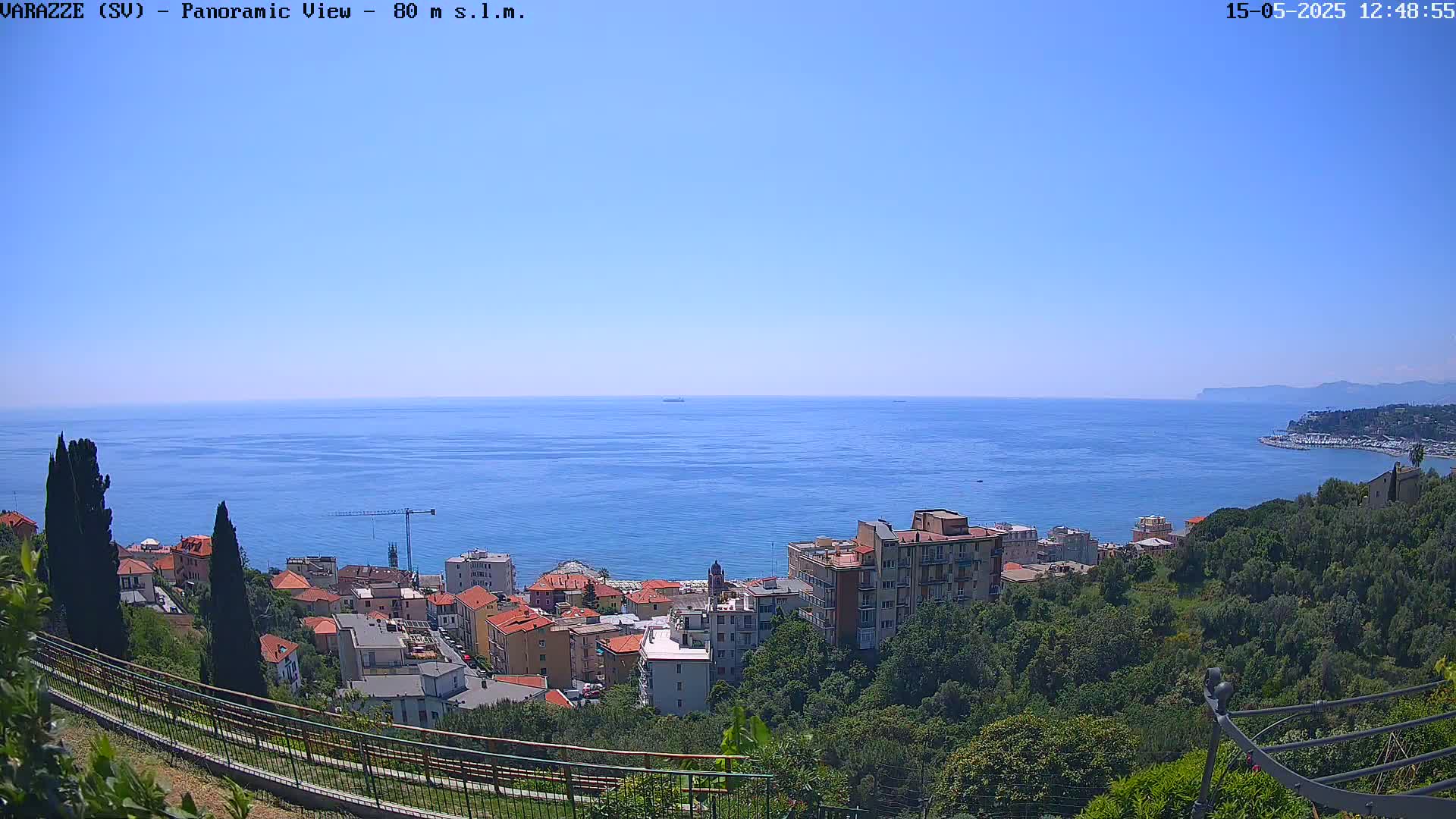 A coastal town overlooks a calm, blue sea on a clear, sunny day.