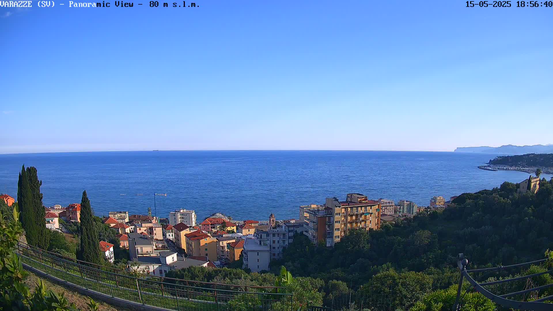 A coastal town with colorful buildings sits on a hillside overlooking a calm blue sea under a clear blue sky.